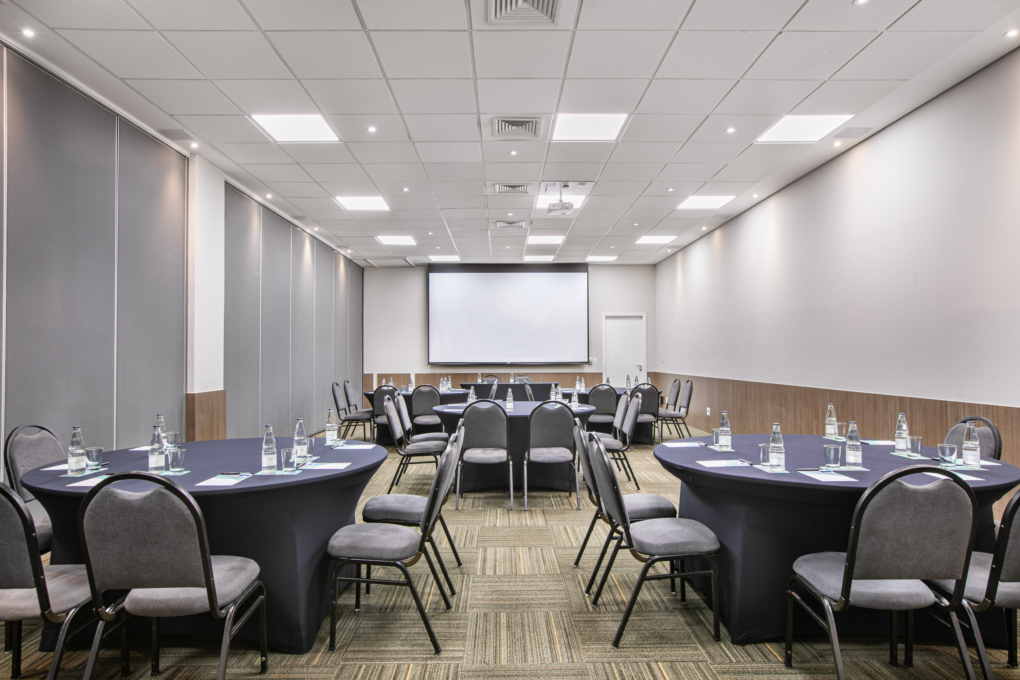 Conference room with round tables, chairs, projector screen, and event setup.