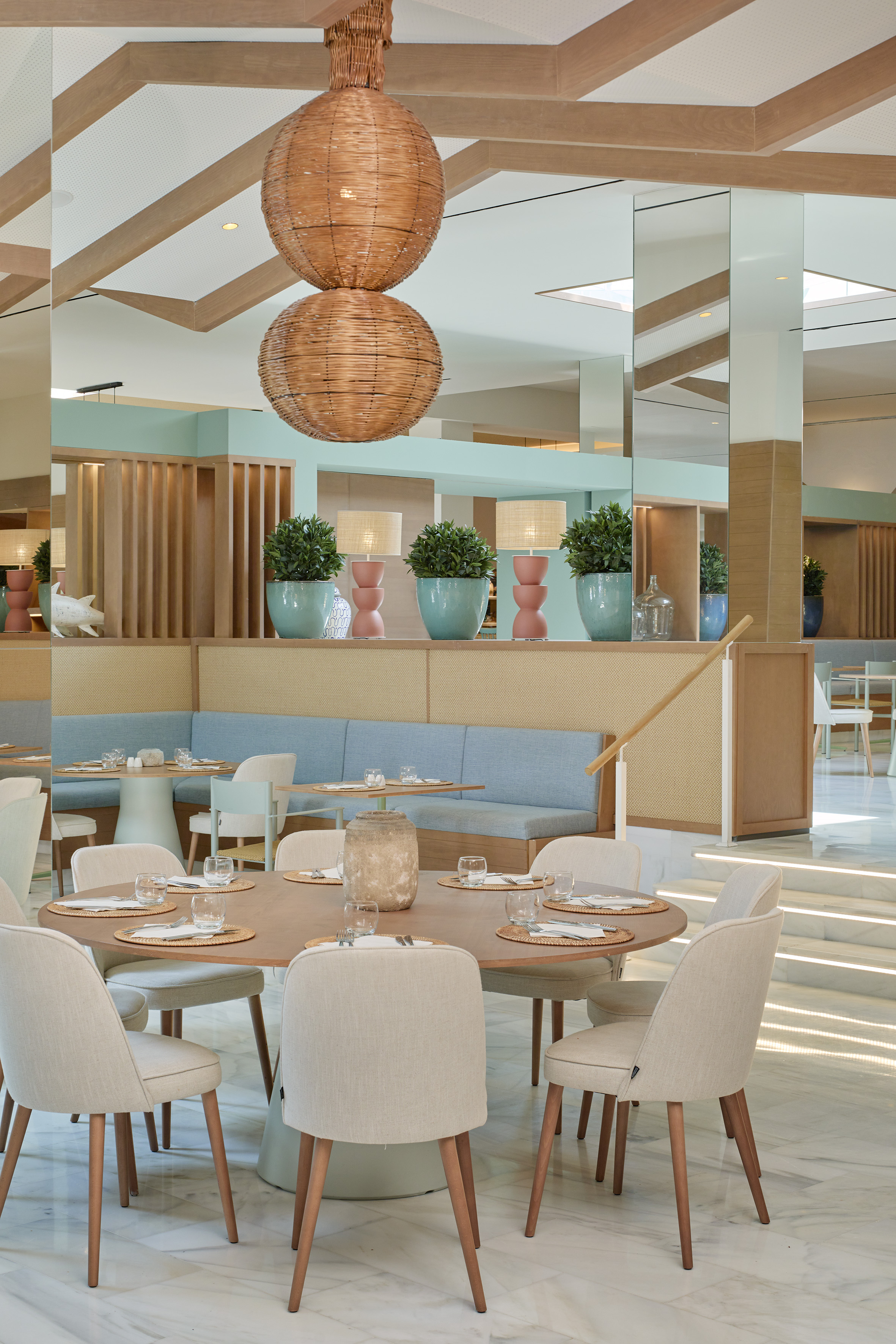 Modern restaurant dining tables, beige chairs, wicker lights, blue booths.