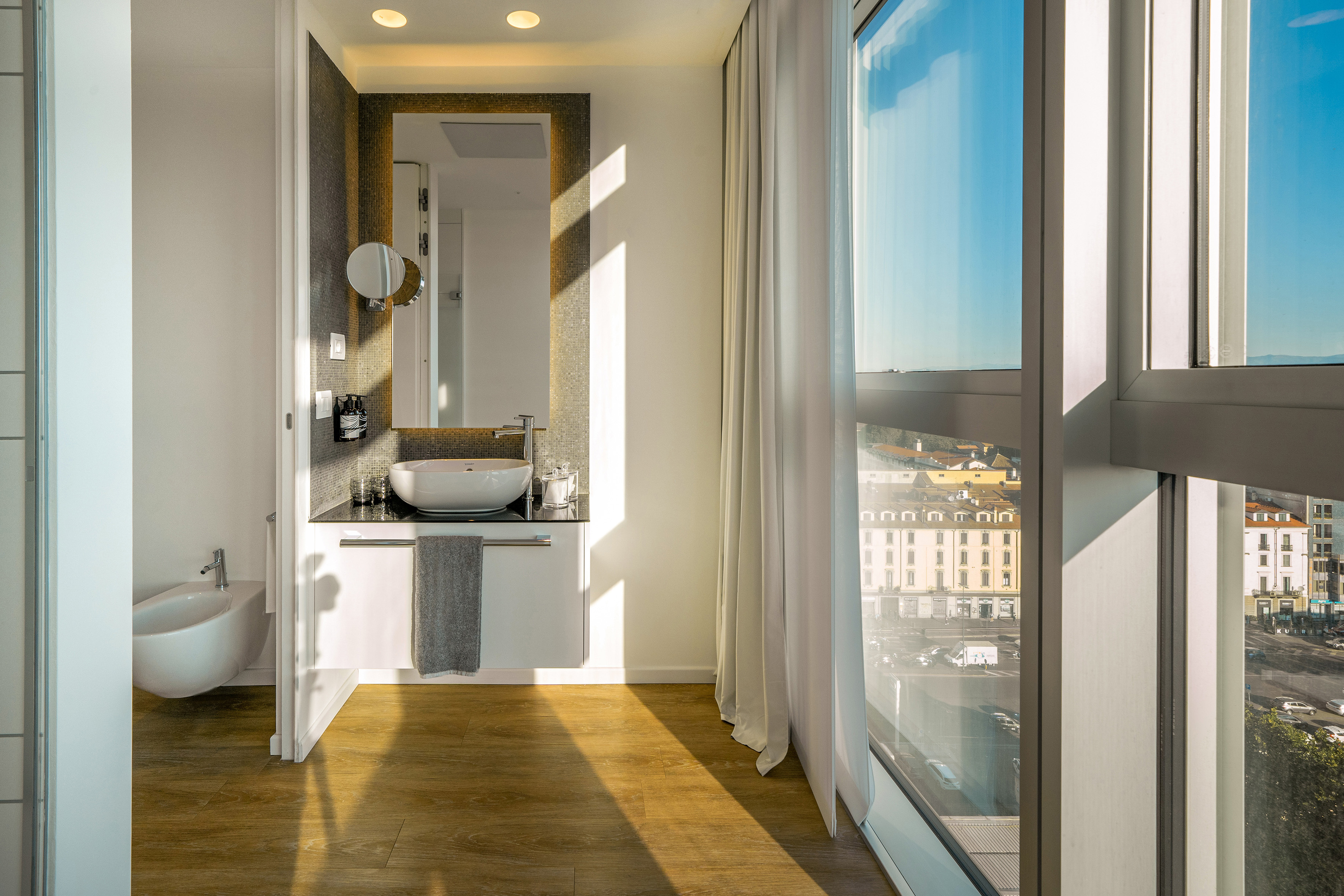 Modern bathroom with bidet, vanity, and city view from a large window.