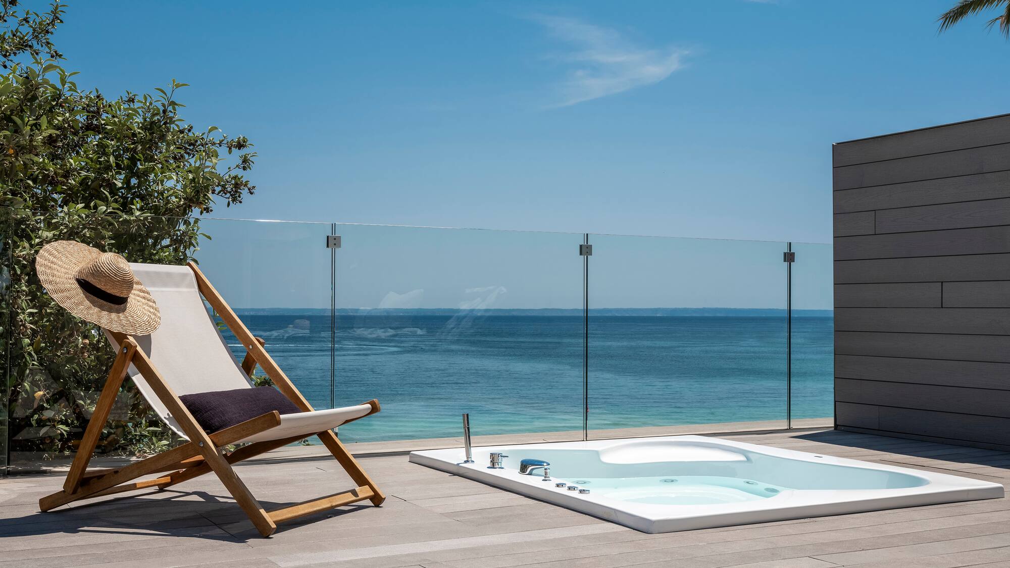 a chair on a deck with a hot tub and a glass fence