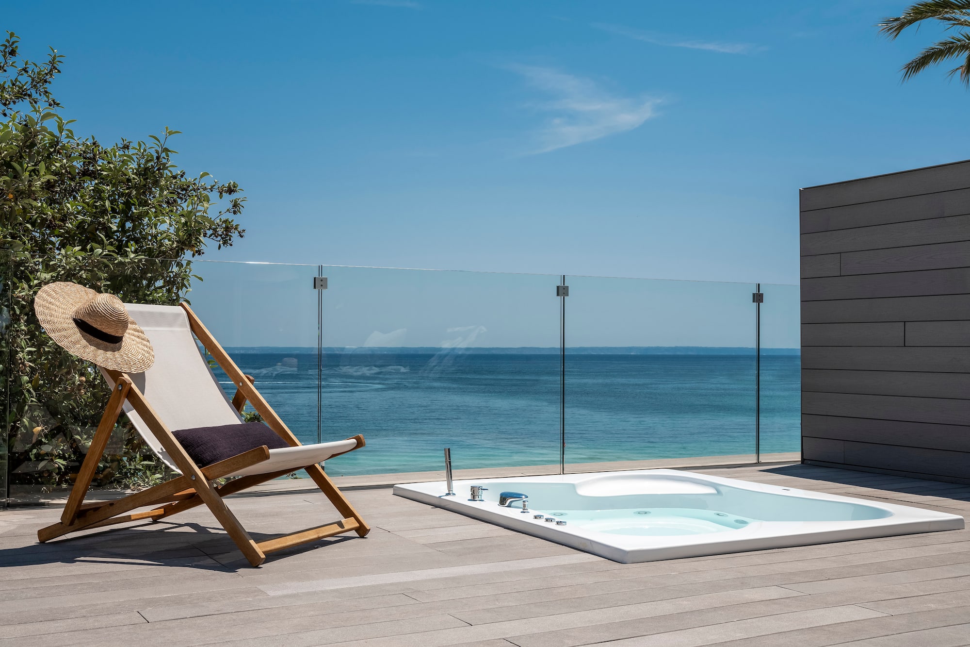 a chair on a deck with a hot tub and a glass fence