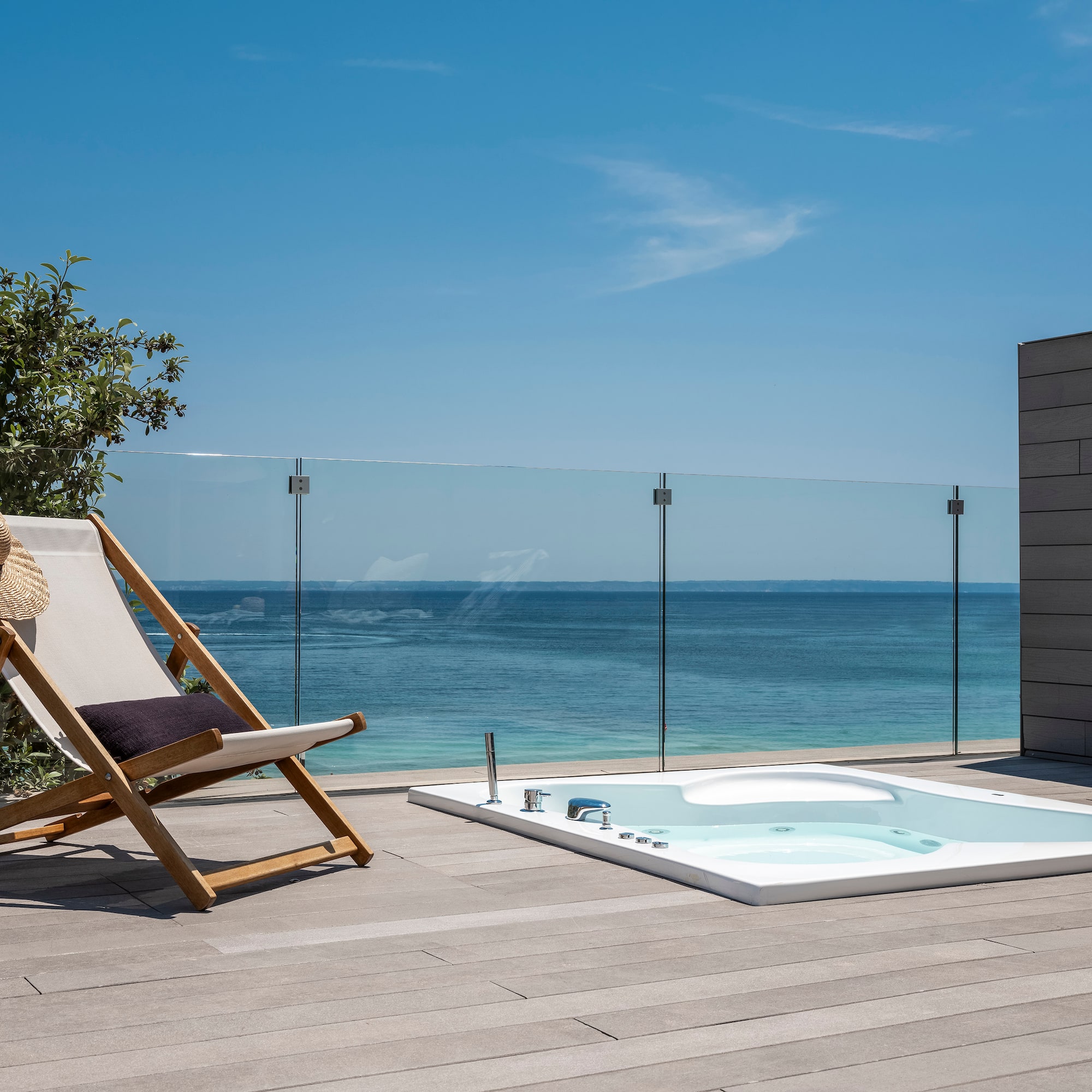 a chair on a deck with a hot tub and a glass fence