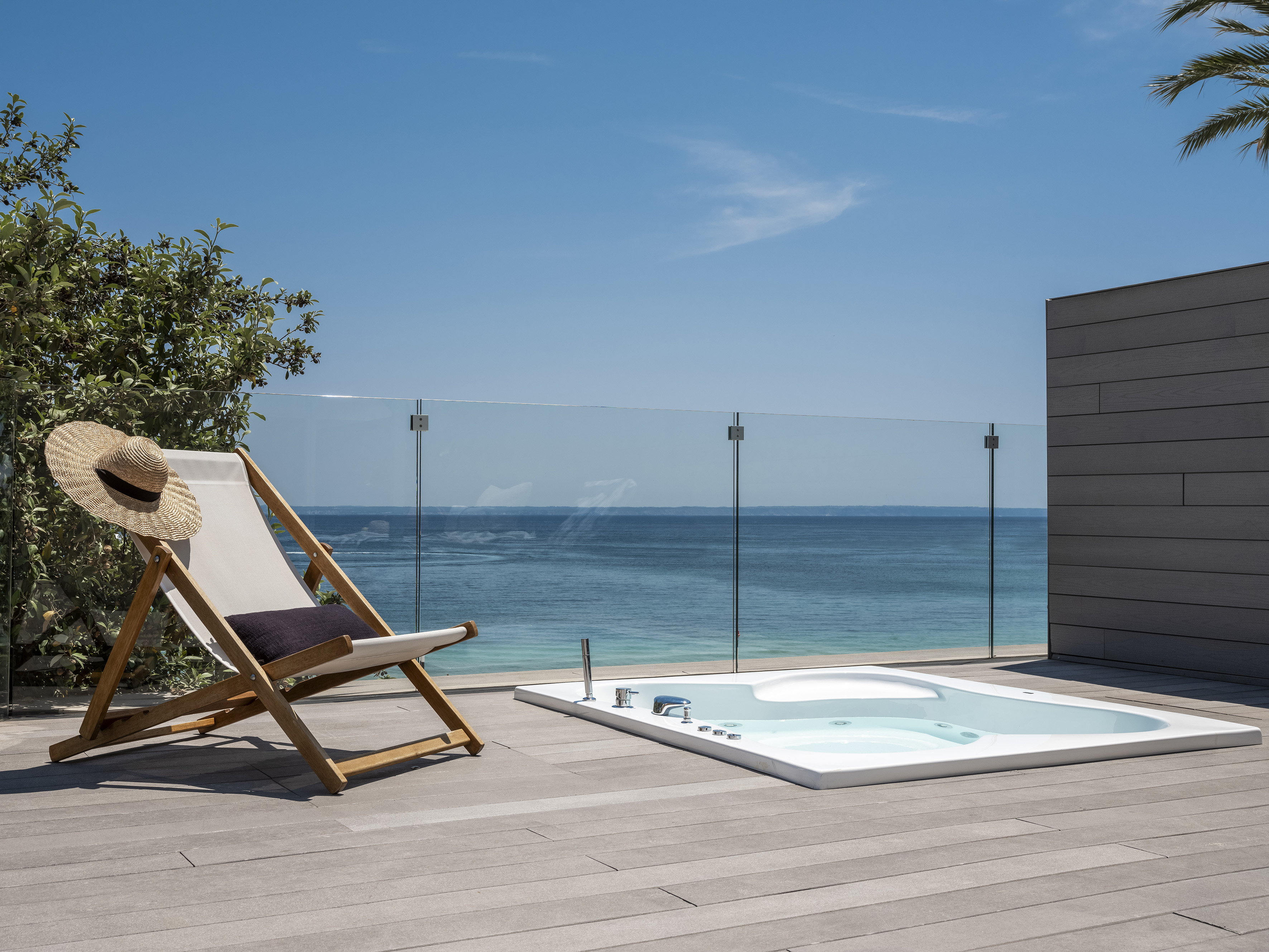Hot tub and deck chair on a luxury terrace with panoramic ocean view.