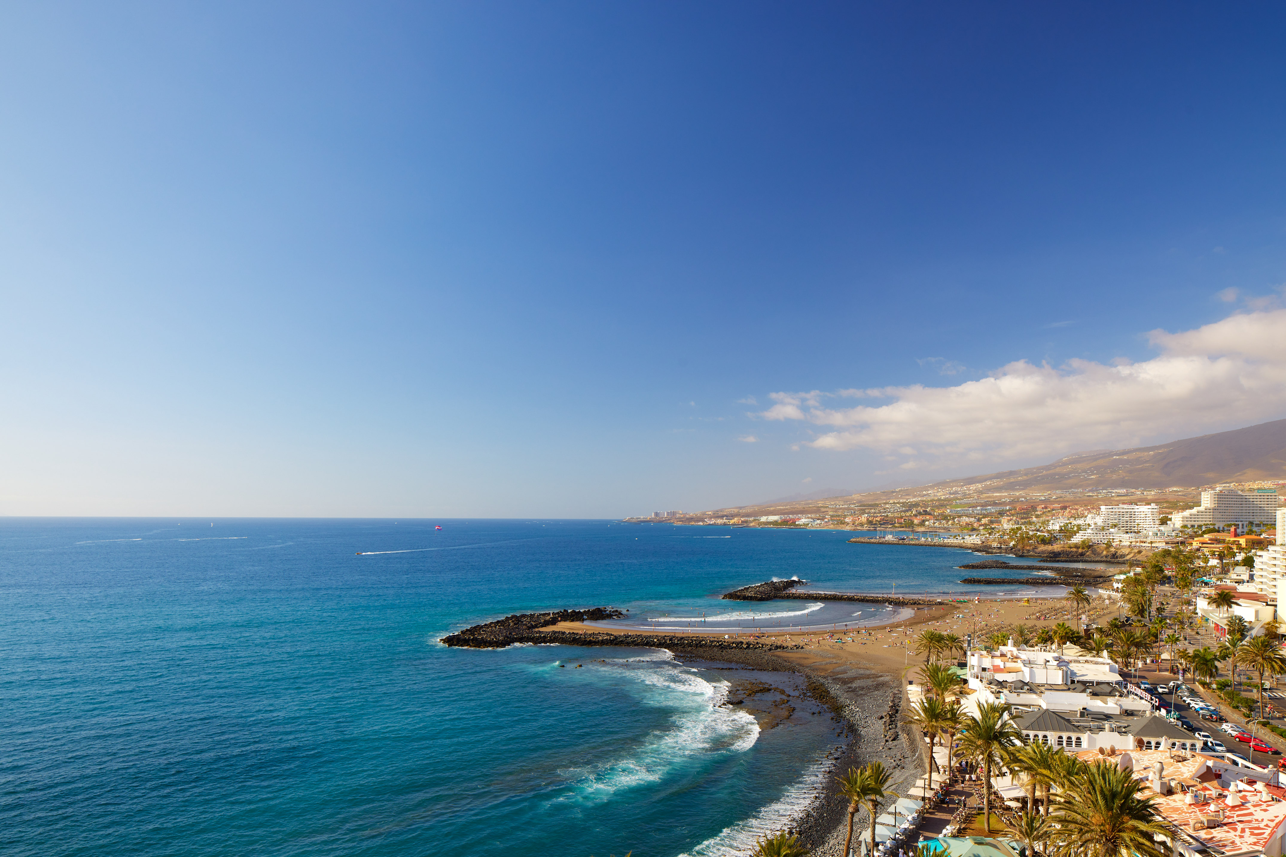 Aerial view of sunny beach, blue ocean, coastal resort town with hotels.