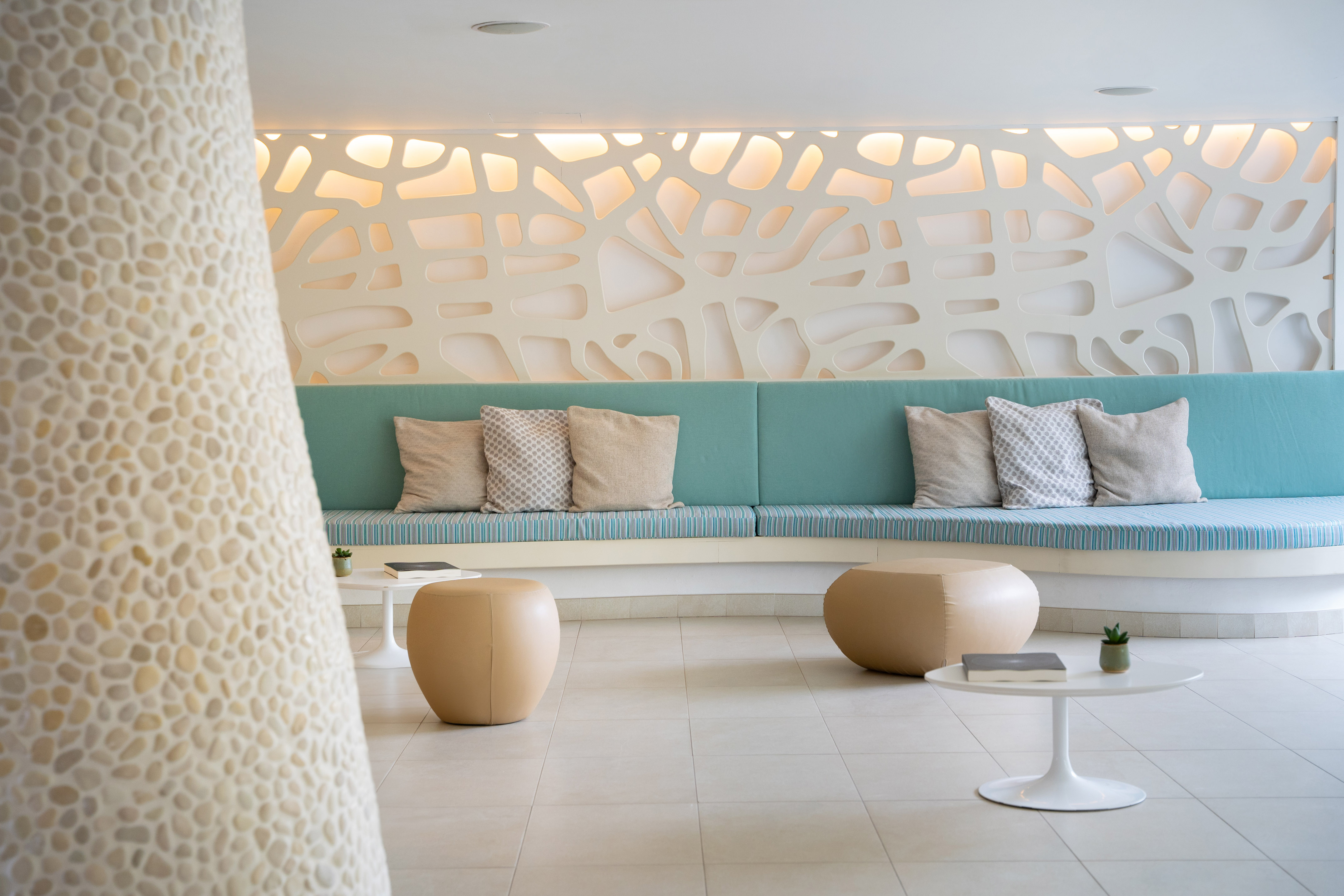 Hotel lobby lounge with curved turquoise bench, modern wall decor, and poufs.