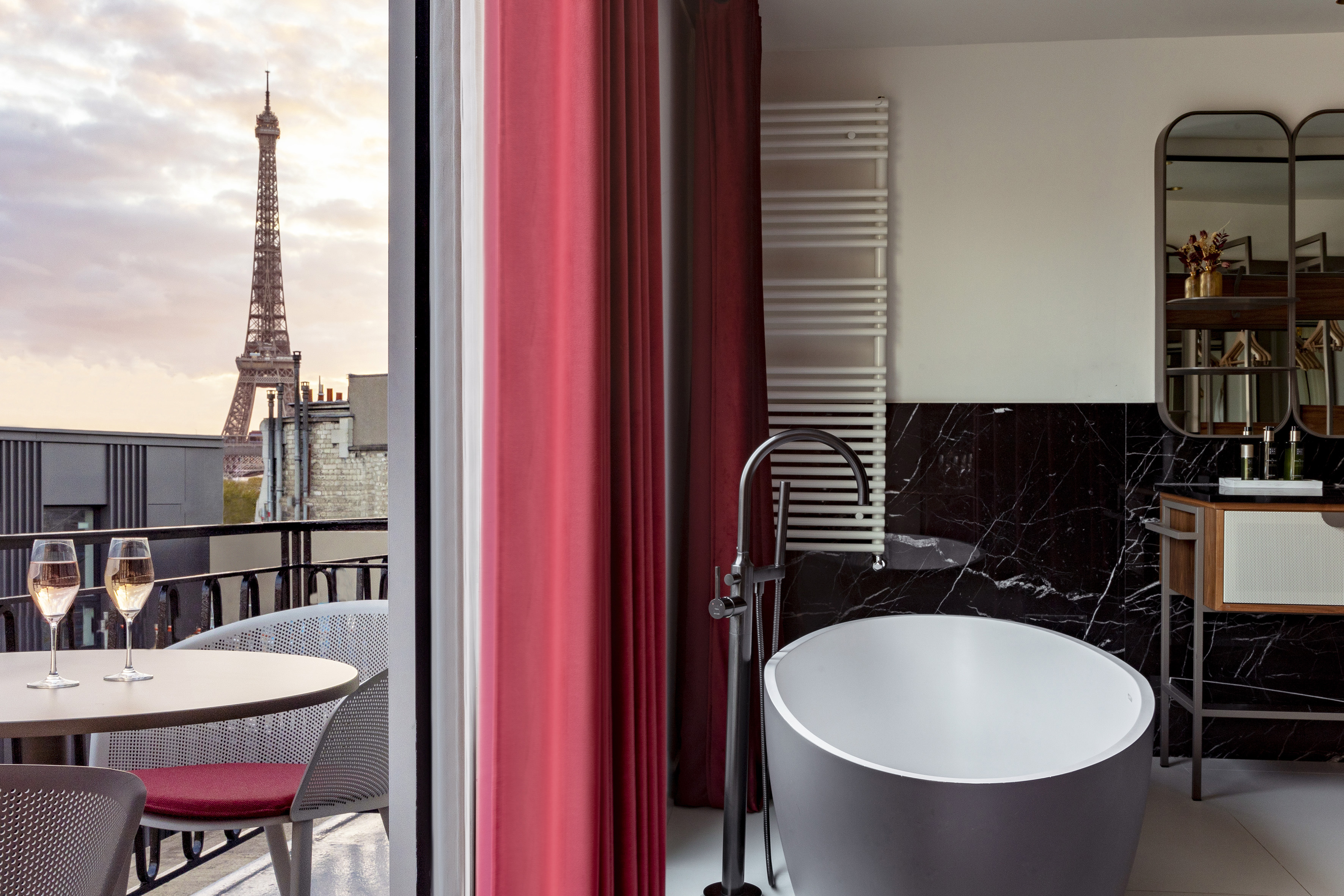 Parisian bathroom with freestanding tub and Eiffel Tower view from balcony.