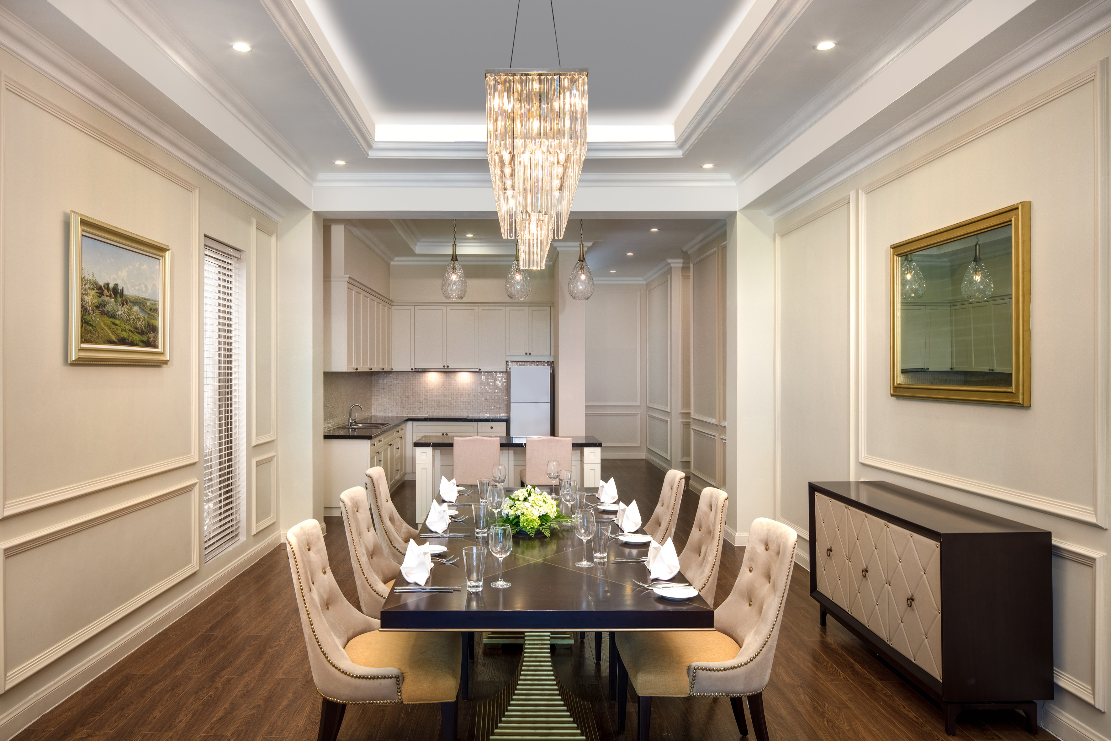 Luxury dining room with set table, tufted chairs, crystal chandelier, kitchen.
