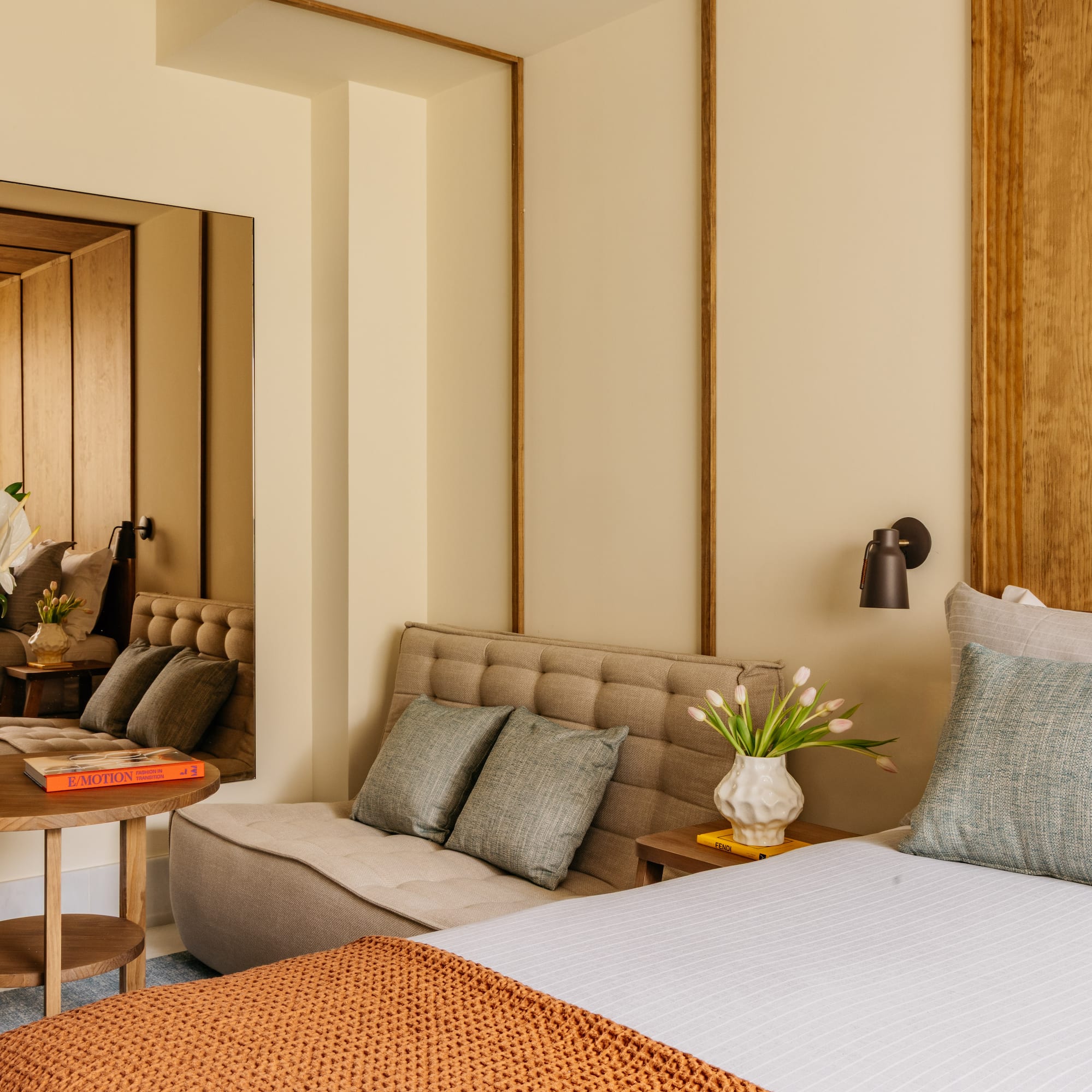 Modern bedroom with wood headboard, tufted daybed, accent tables, and decor.