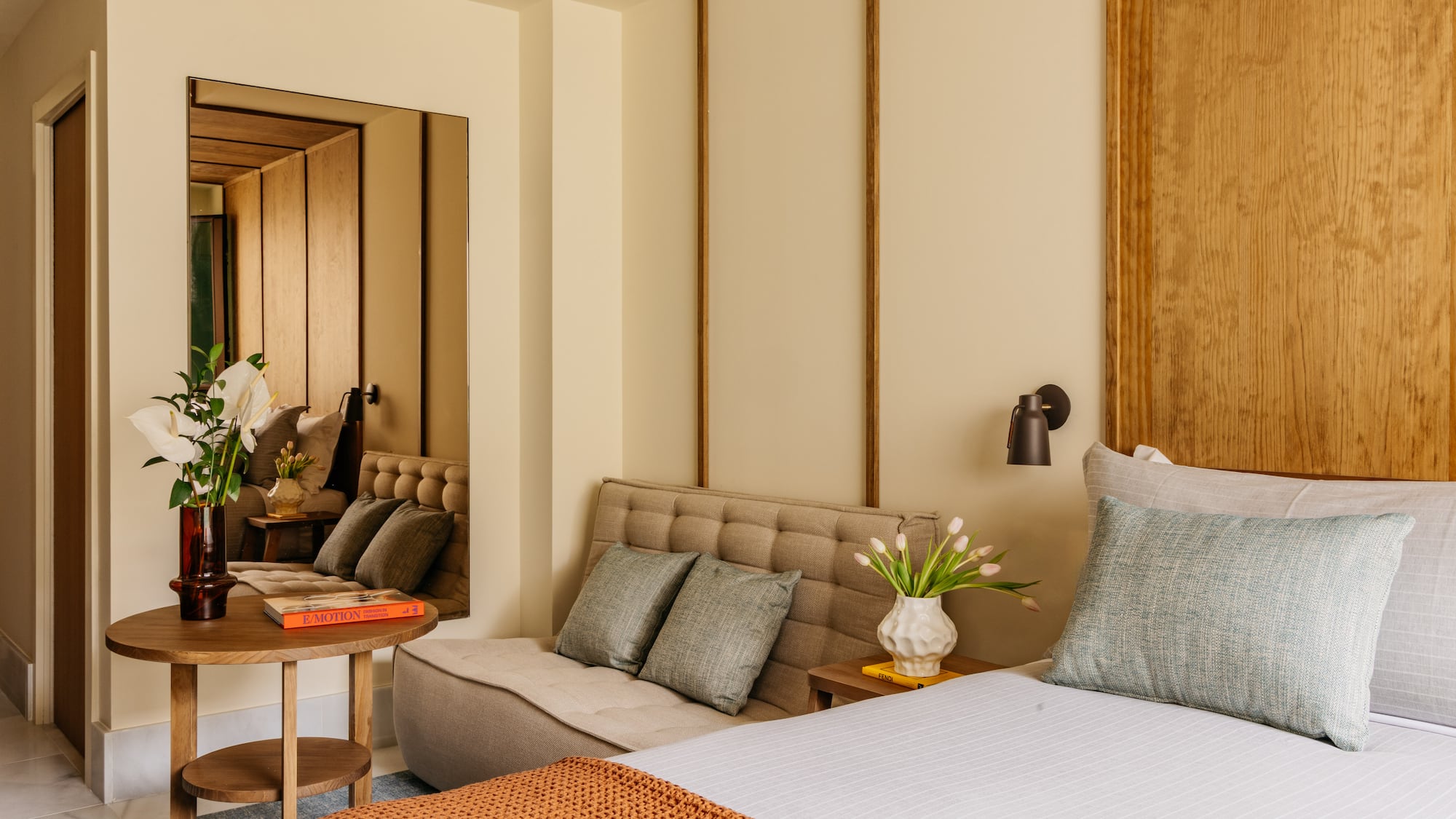 Modern bedroom with wood headboard, tufted daybed, accent tables, and decor.