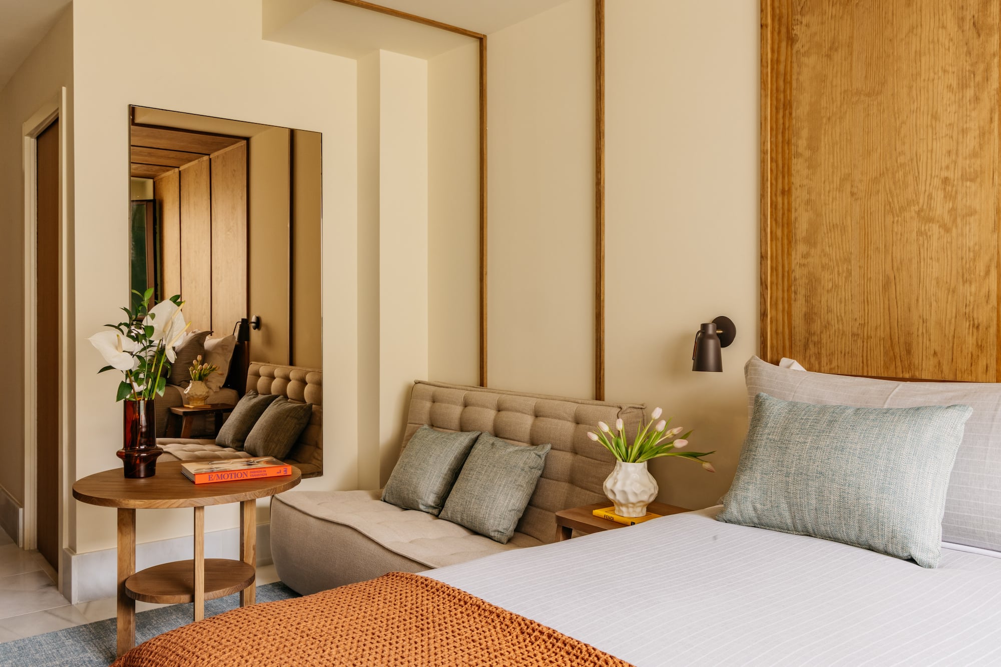 Modern bedroom with wood headboard, tufted daybed, accent tables, and decor.