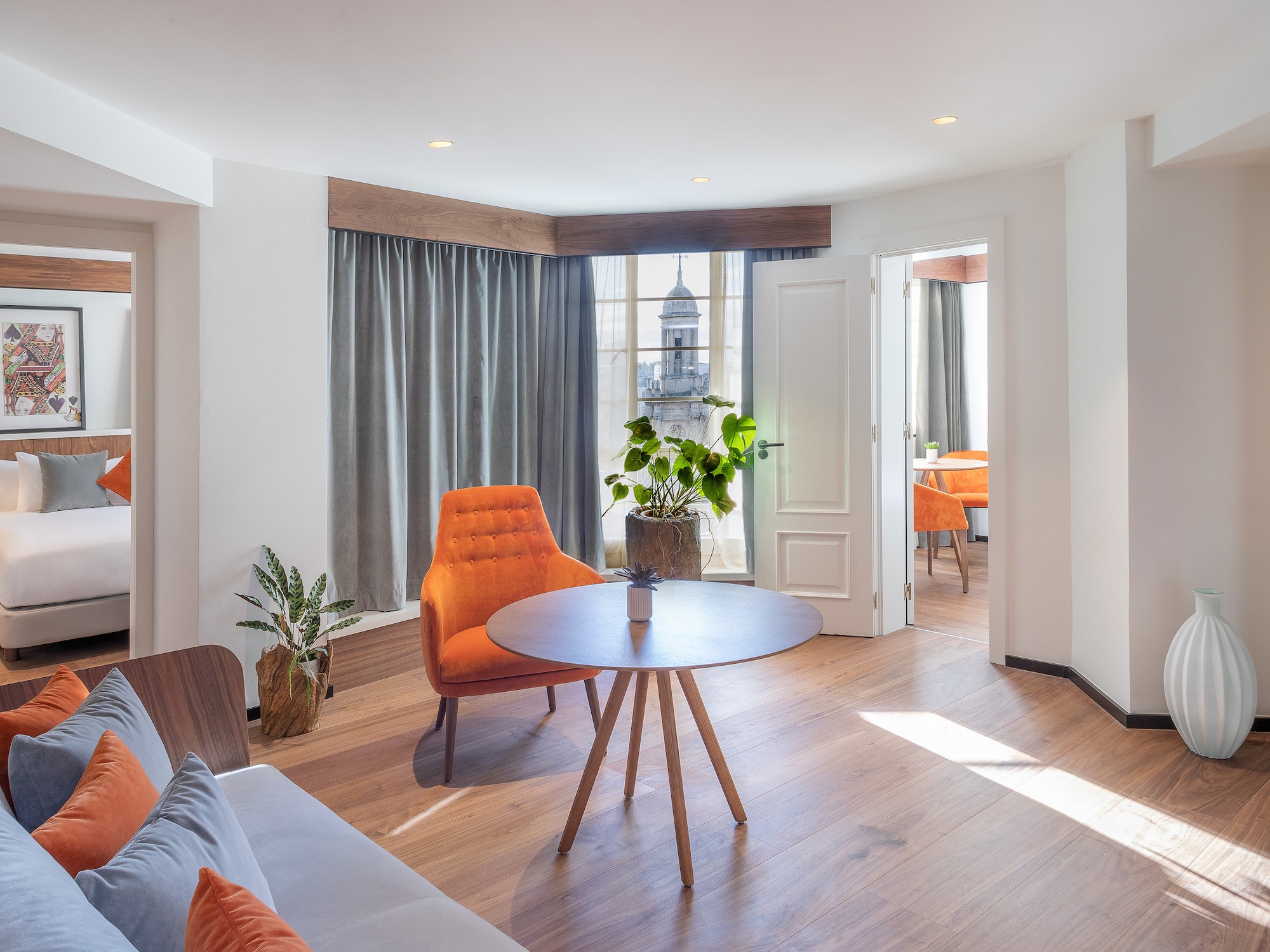 Stylish hotel suite: living area with orange chair, bedroom, and city view.