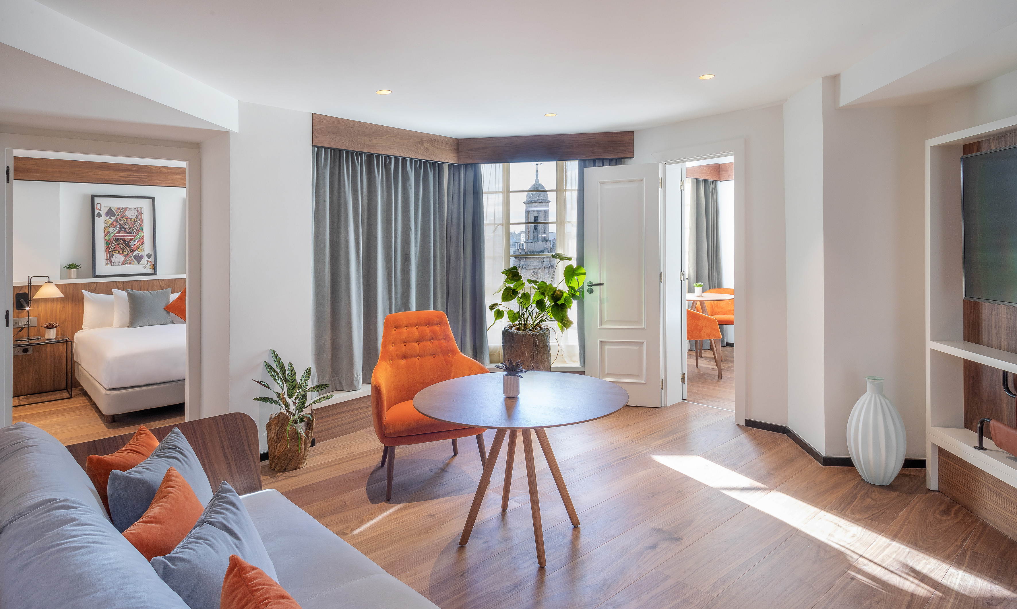 Modern hotel suite with lounge, bedroom, orange decor, and historic city view.