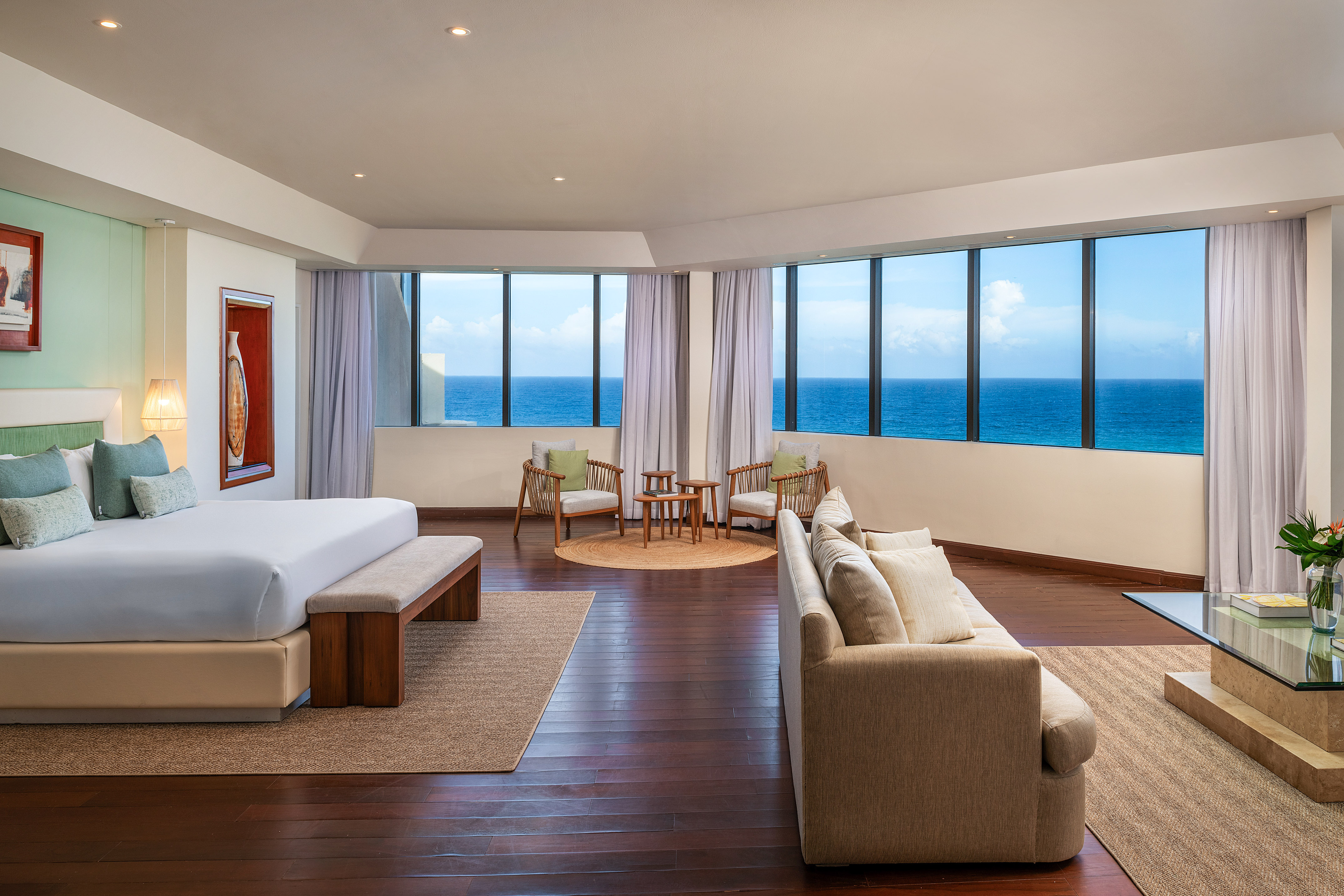 Luxury ocean view hotel suite with king bed, sofa, and floor-to-ceiling windows.