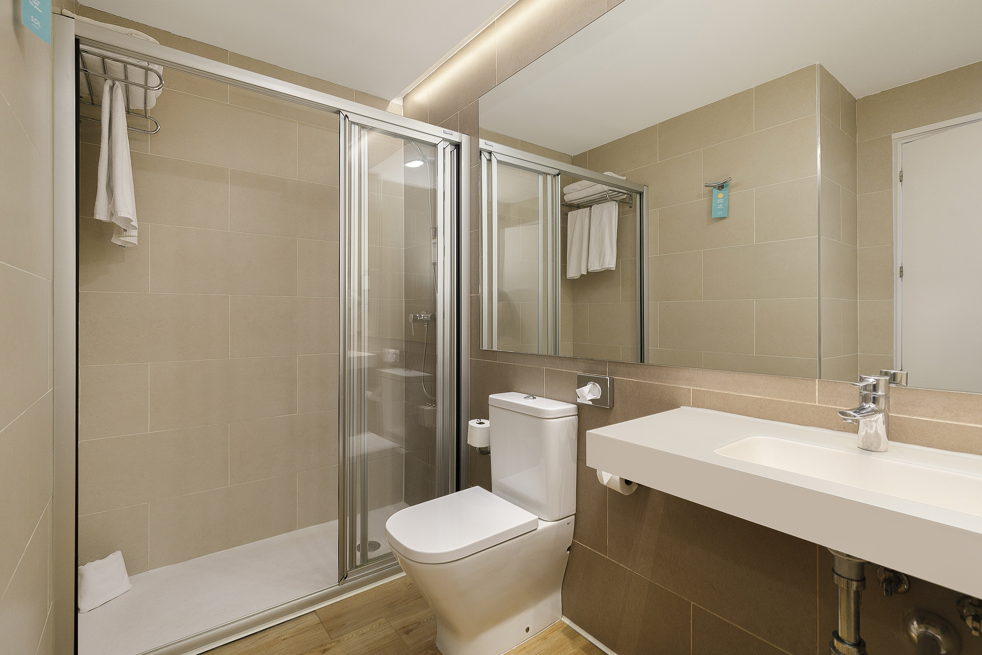 Modern beige tiled bathroom with glass shower, white toilet, and sink.