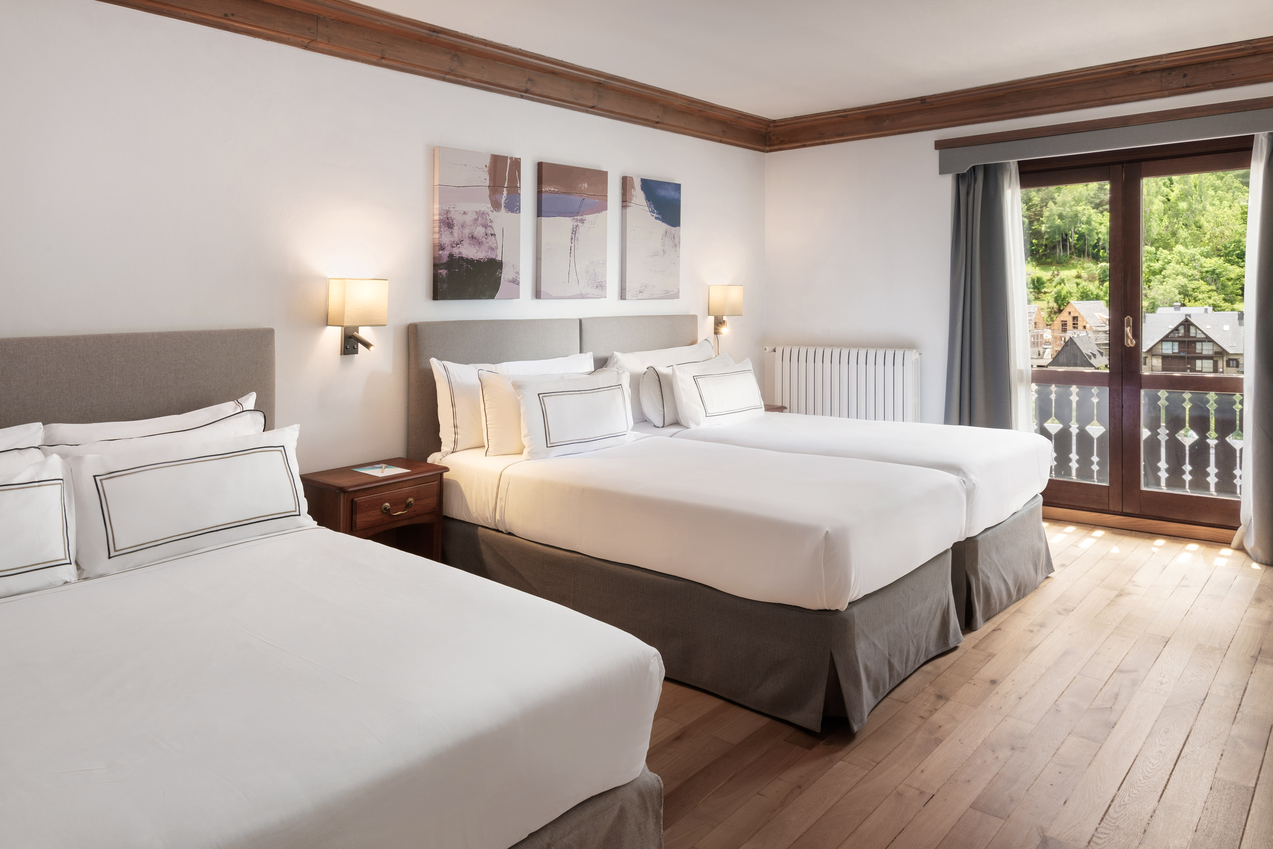 Triple hotel room with wooden floor, white beds, and balcony mountain view.
