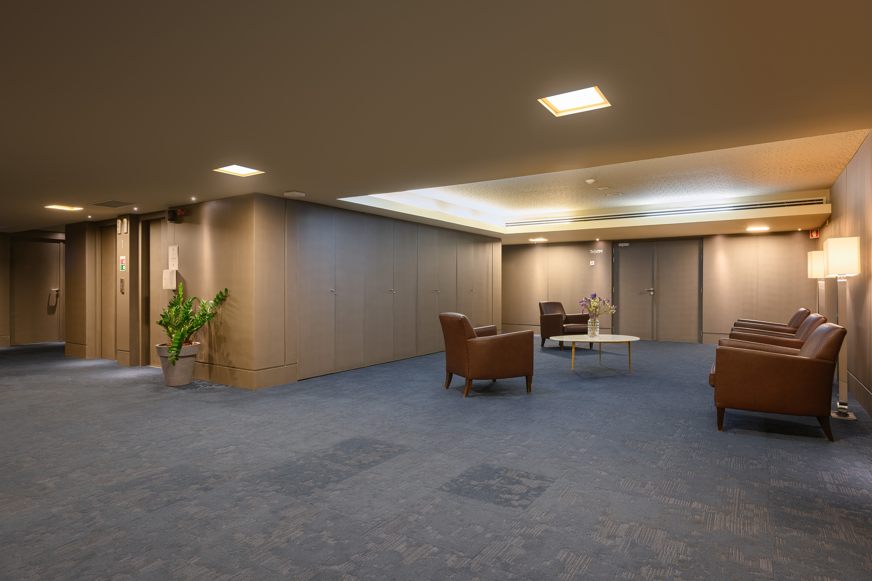 Modern hotel lobby with brown leather armchairs, blue carpet, and warm lighting.