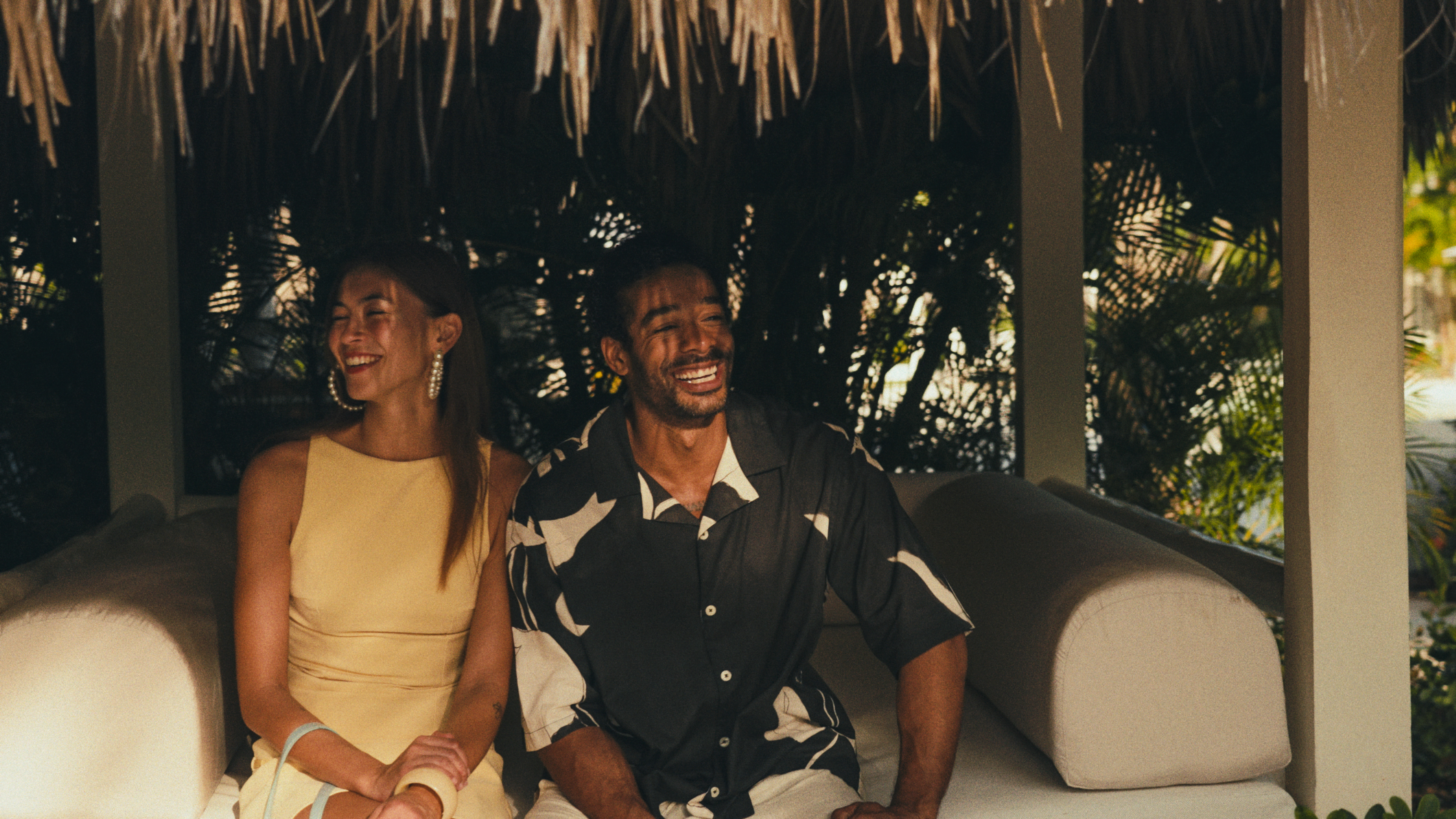 Smiling couple relaxing in a tropical resort cabana lounge.