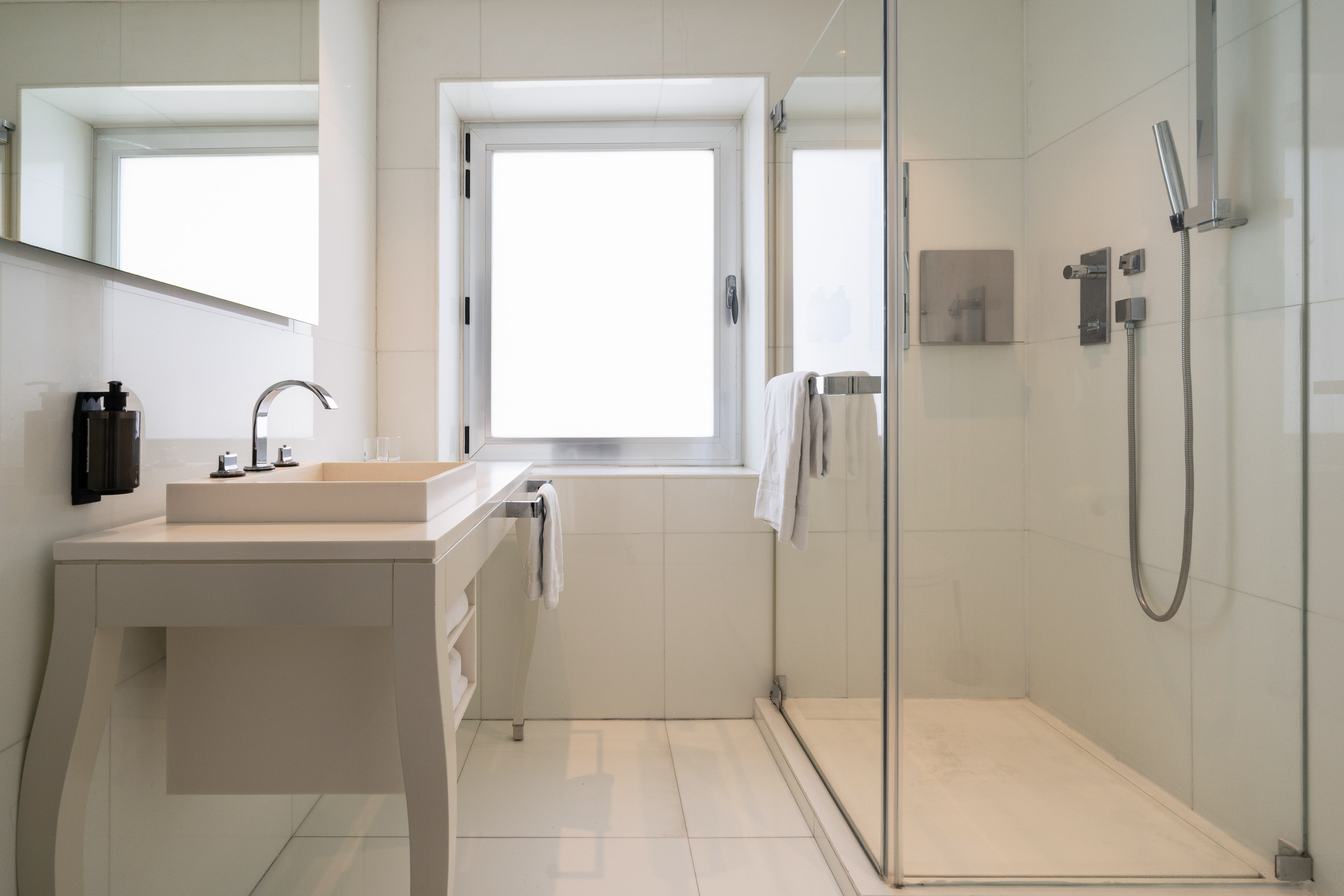 Modern white tiled bathroom with glass shower, vanity sink, and window.