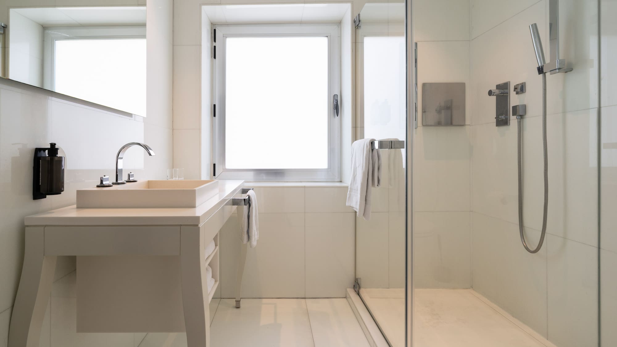 Modern white tiled bathroom with glass shower, vanity sink, and window.
