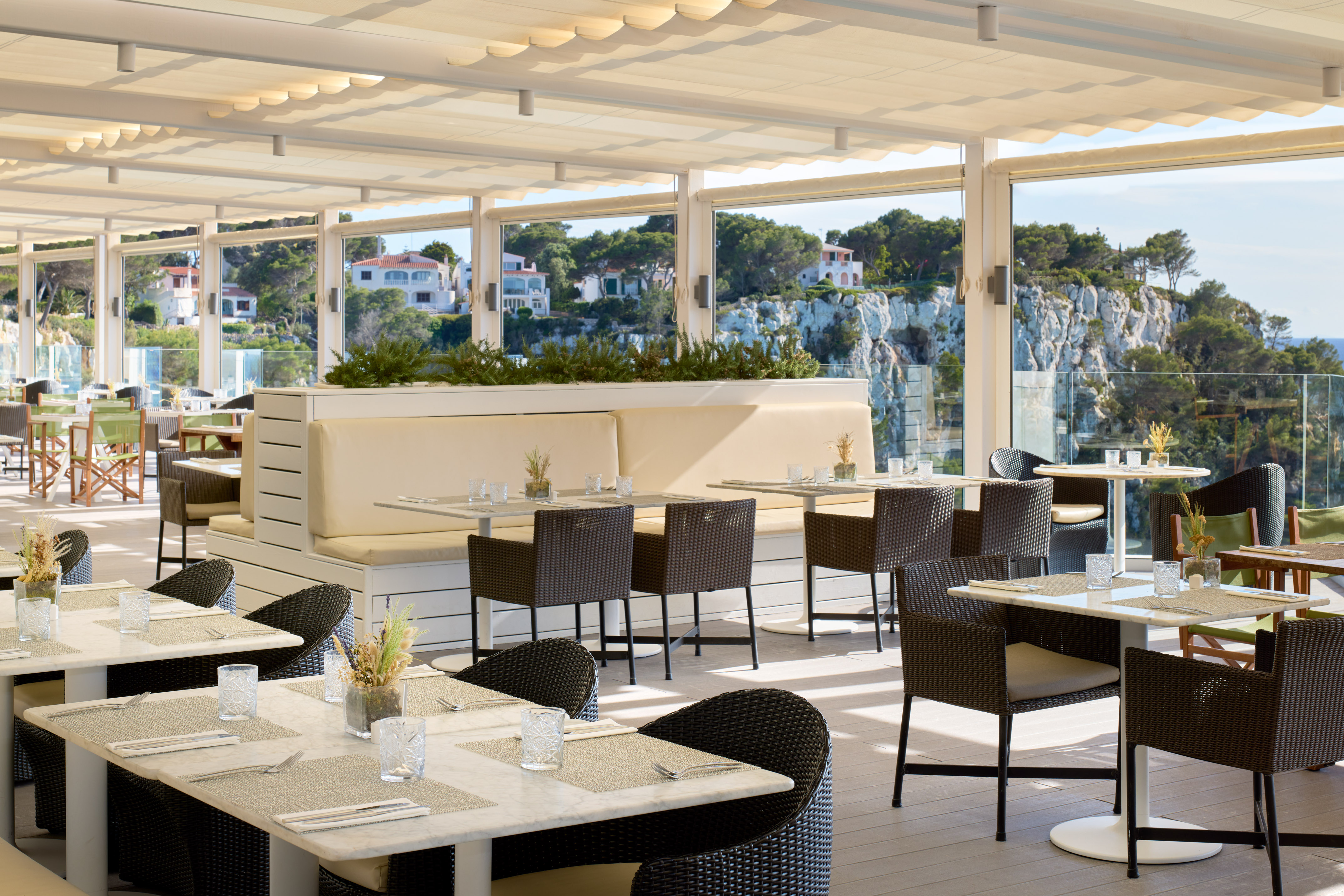 Bright modern restaurant terrace with sea view and coastal cliffside homes.