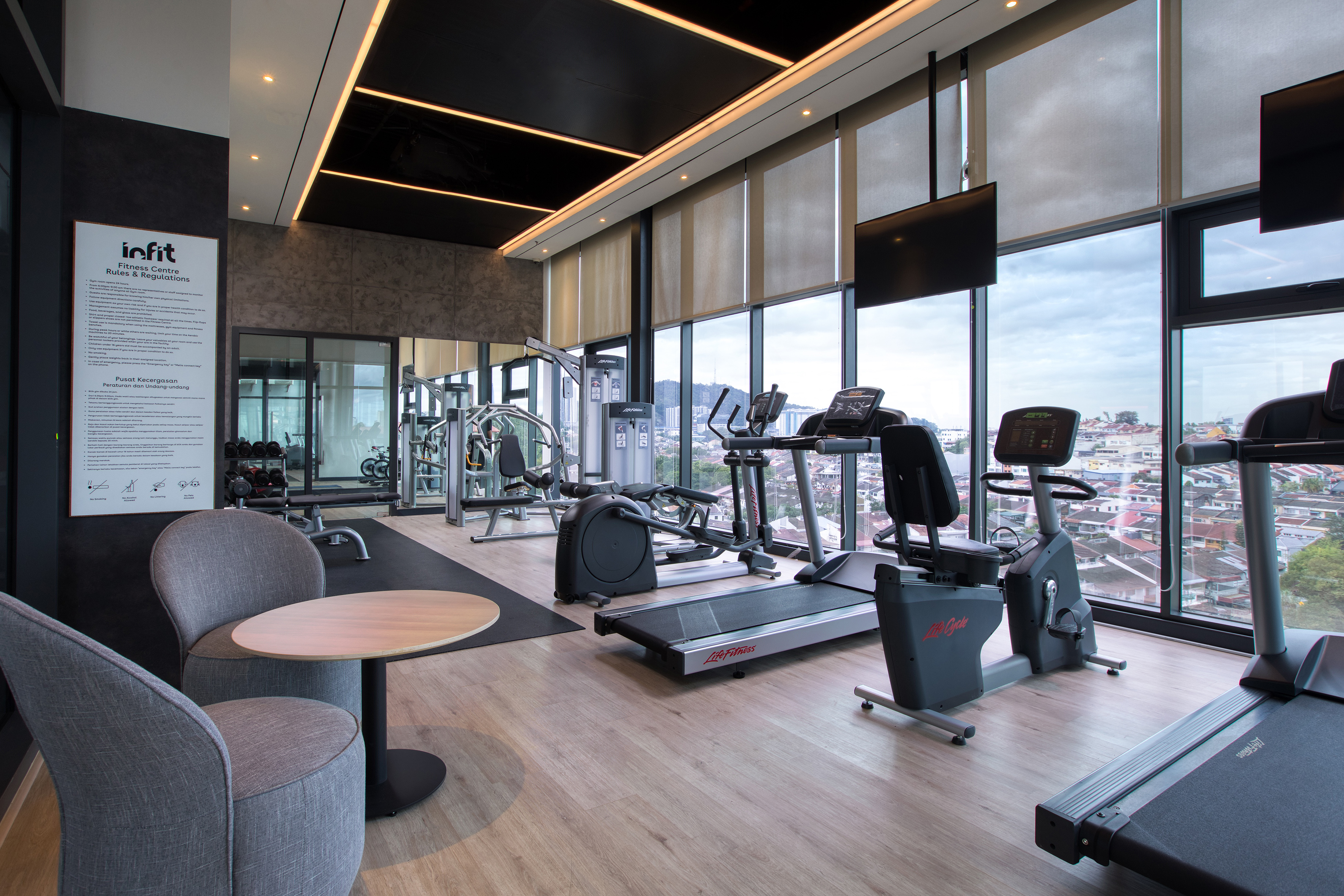Modern gym with cardio and weight machines, city view, and lounge seating.