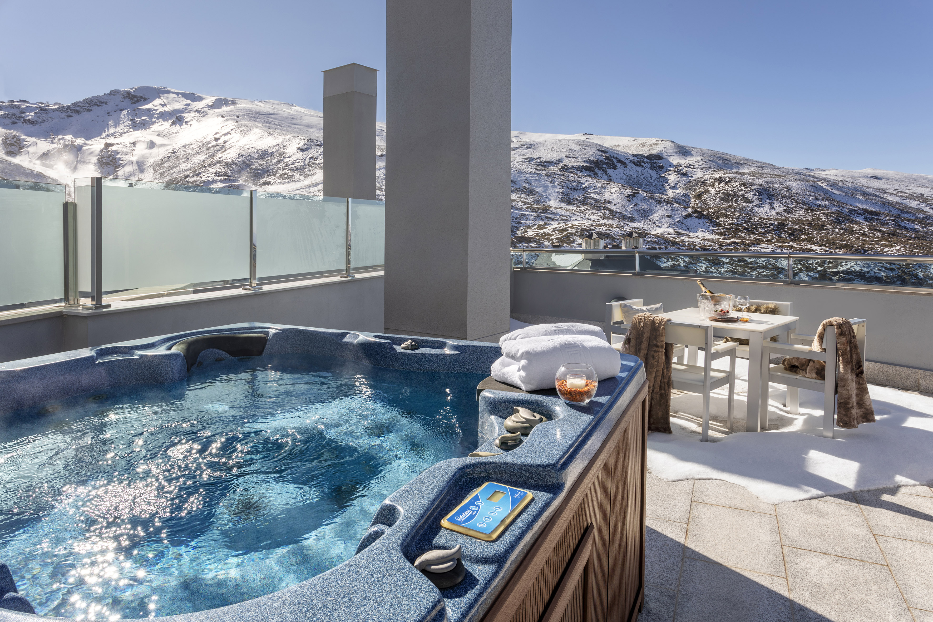 Luxury outdoor hot tub on a winter balcony overlooking snowy mountains.