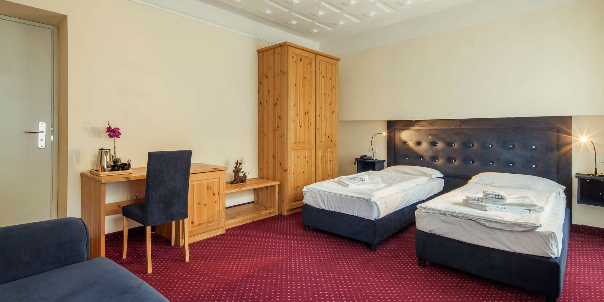 Twin hotel room with two beds, red carpet, wooden wardrobe, and desk.