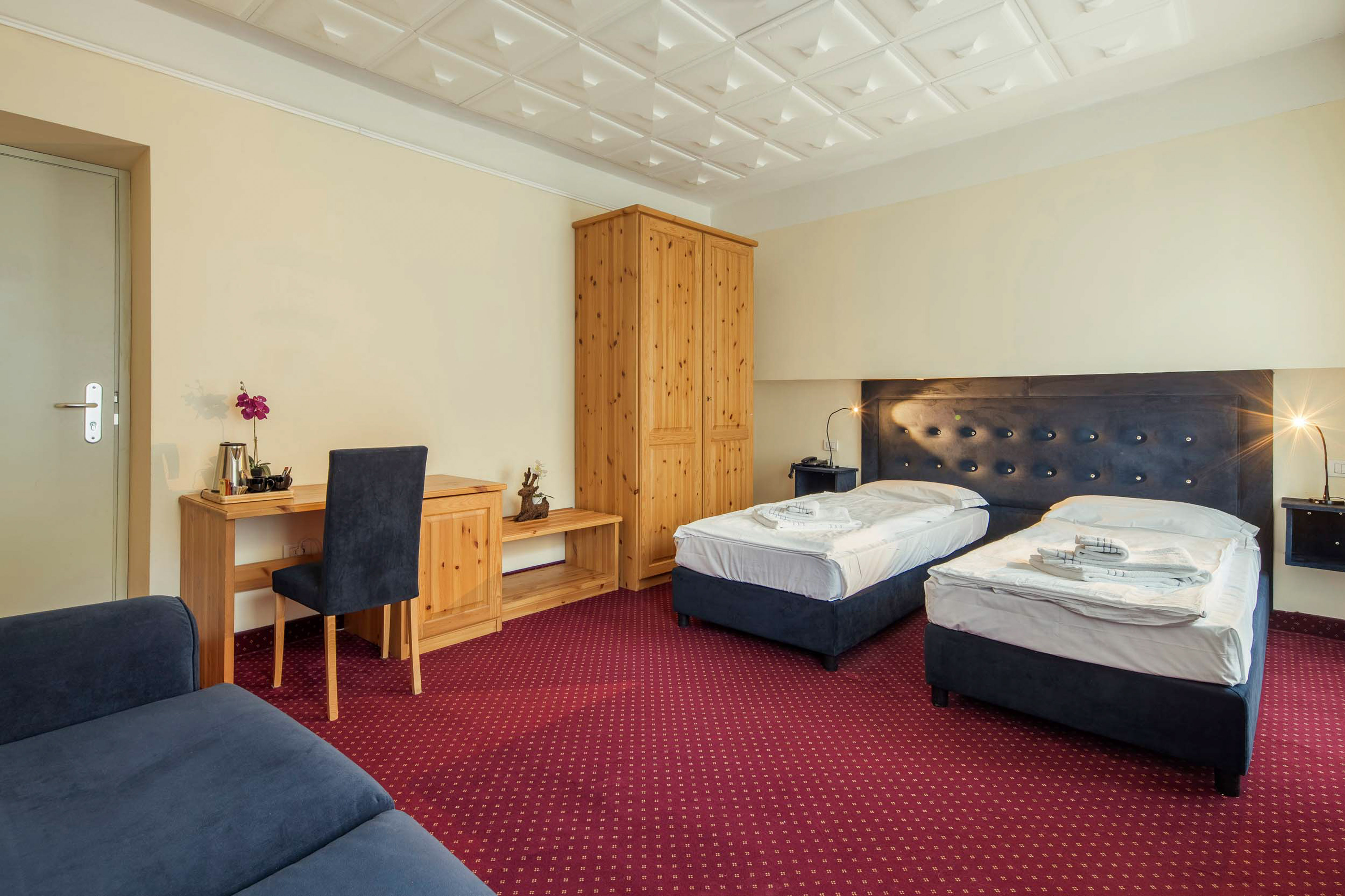 Twin hotel room with two beds, red carpet, wooden wardrobe, and desk.