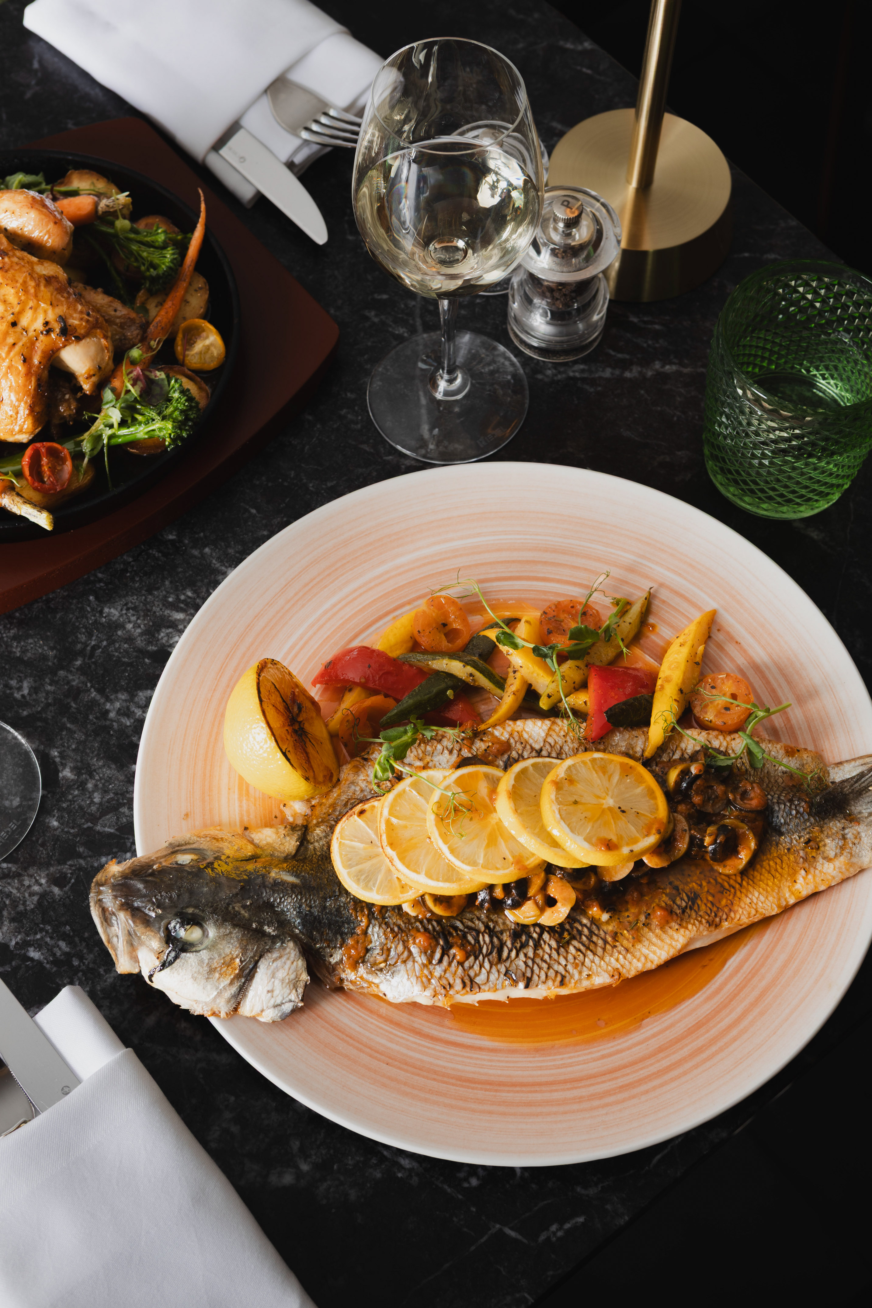 Roasted whole fish with lemon, mixed vegetables, white wine, and another entree.