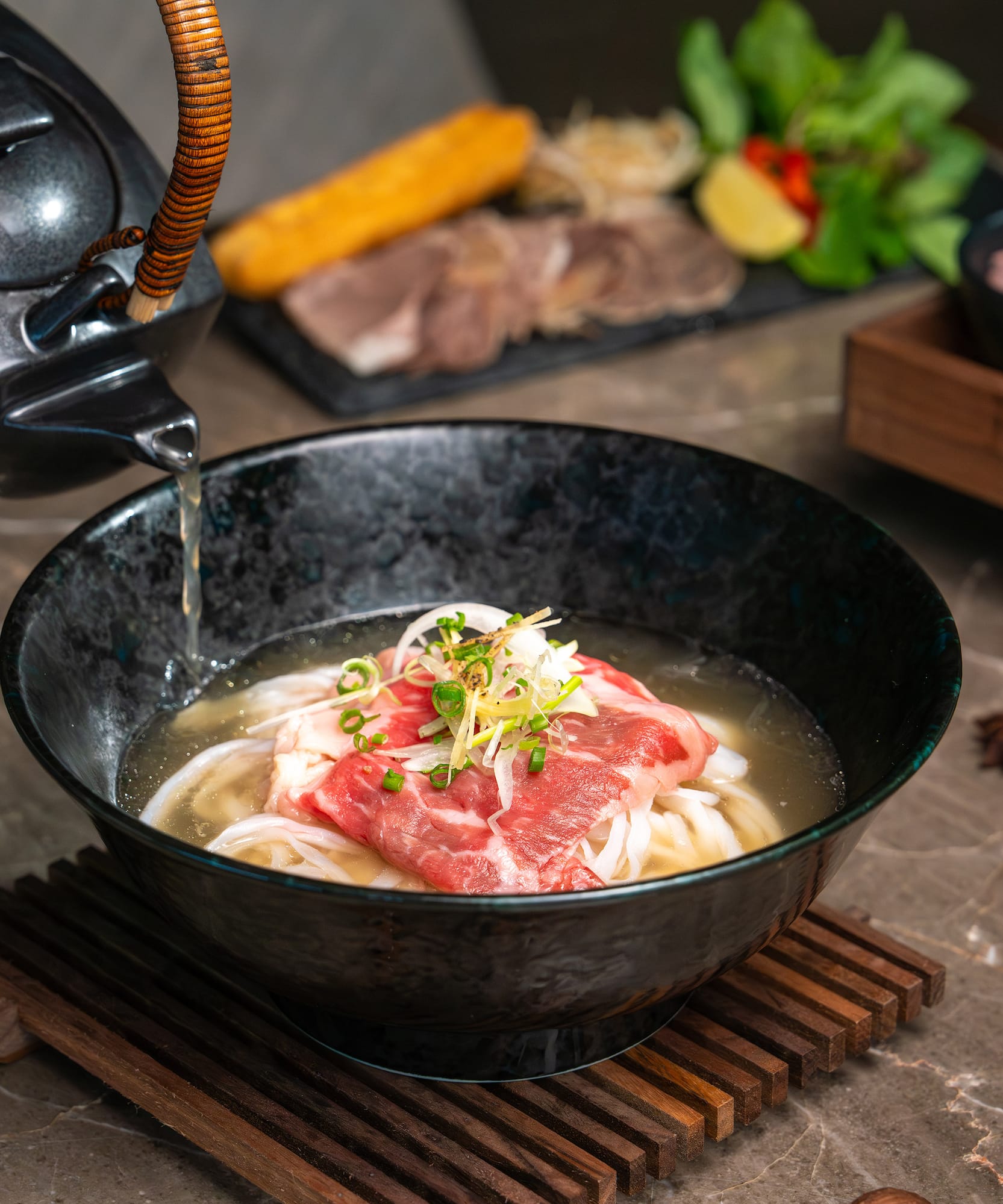 a bowl of soup with meat and noodles being poured into a teapot
