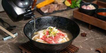 a bowl of soup with meat and noodles being poured into a teapot