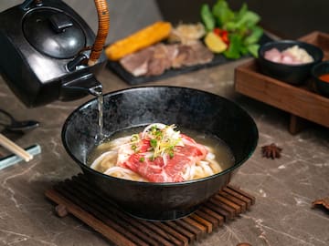 a bowl of soup with meat and noodles being poured into a teapot