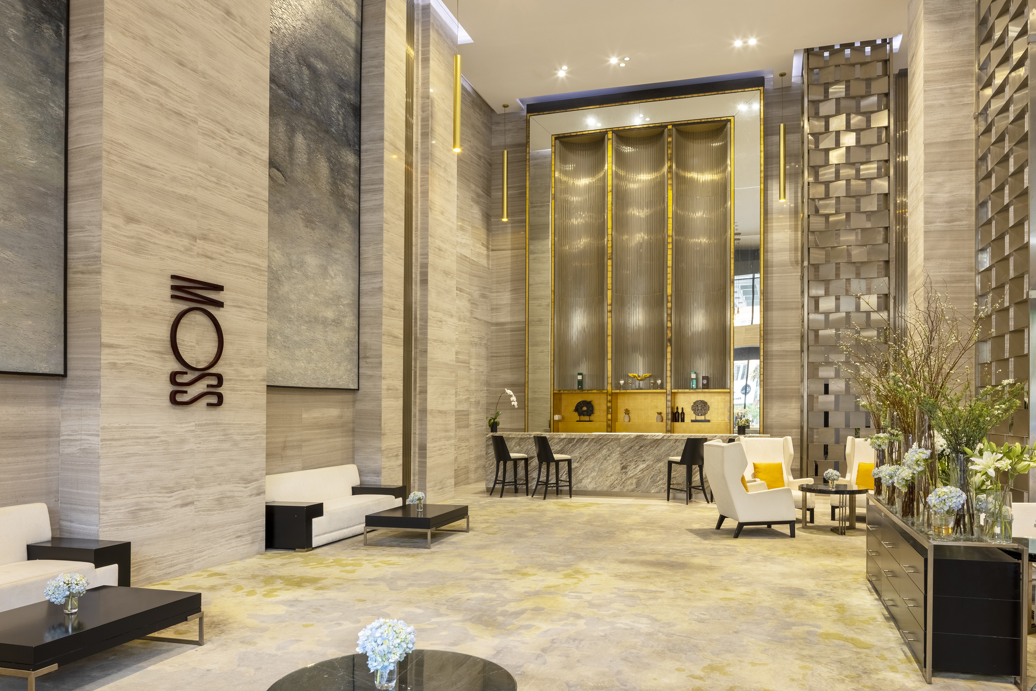 Luxurious modern hotel lobby with "MOSS" sign, marble bar, and lounge seating.