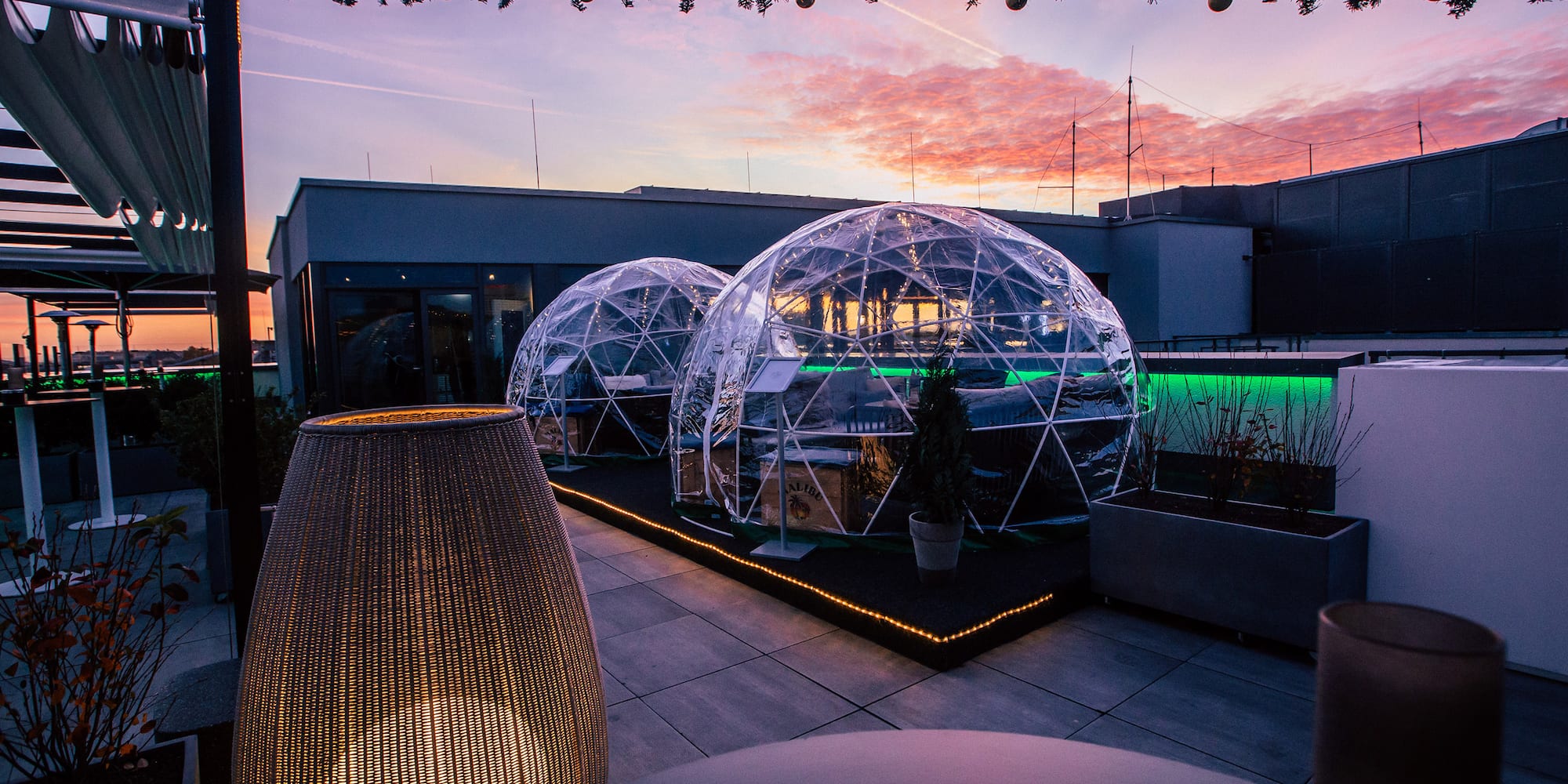 Rooftop terrace with illuminated dining igloos, festive decor, and sunset.