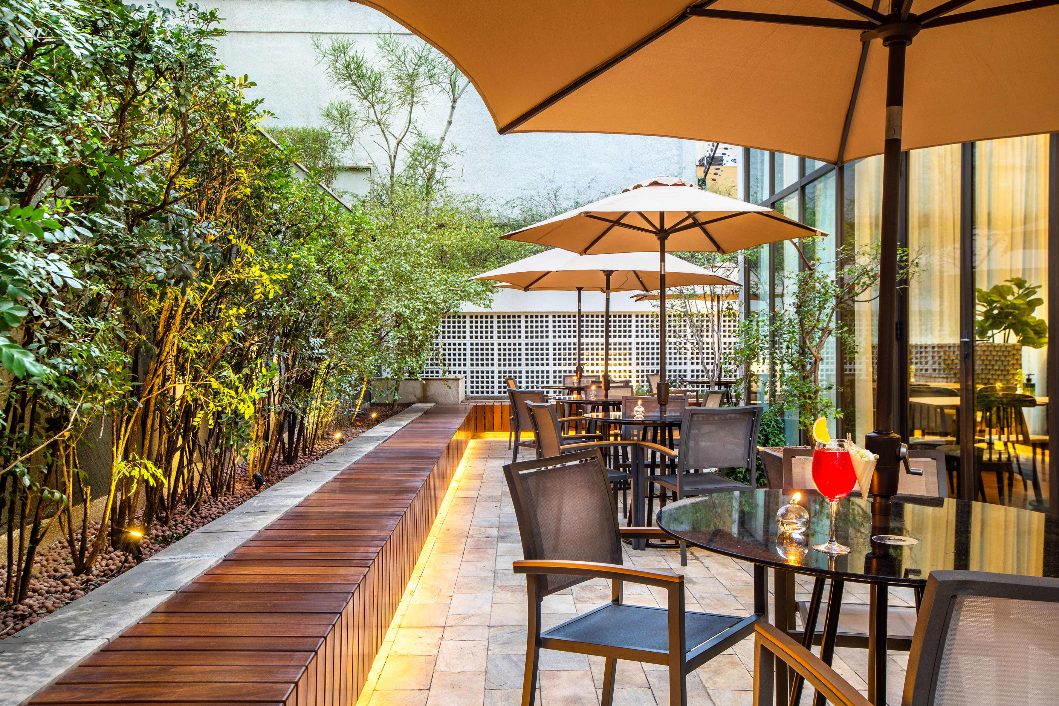 Hotel patio with shaded tables, umbrellas, and illuminated green foliage.