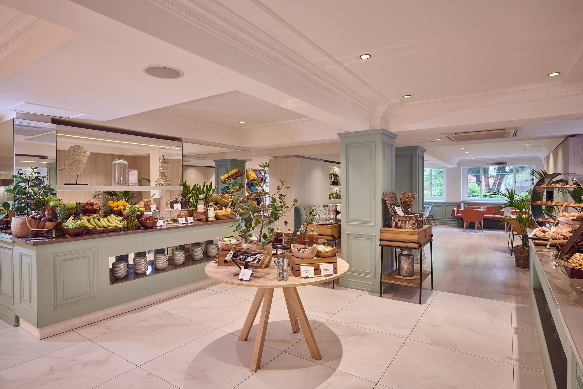 Bright hotel breakfast buffet with fresh fruit, pastries, and spacious dining area.