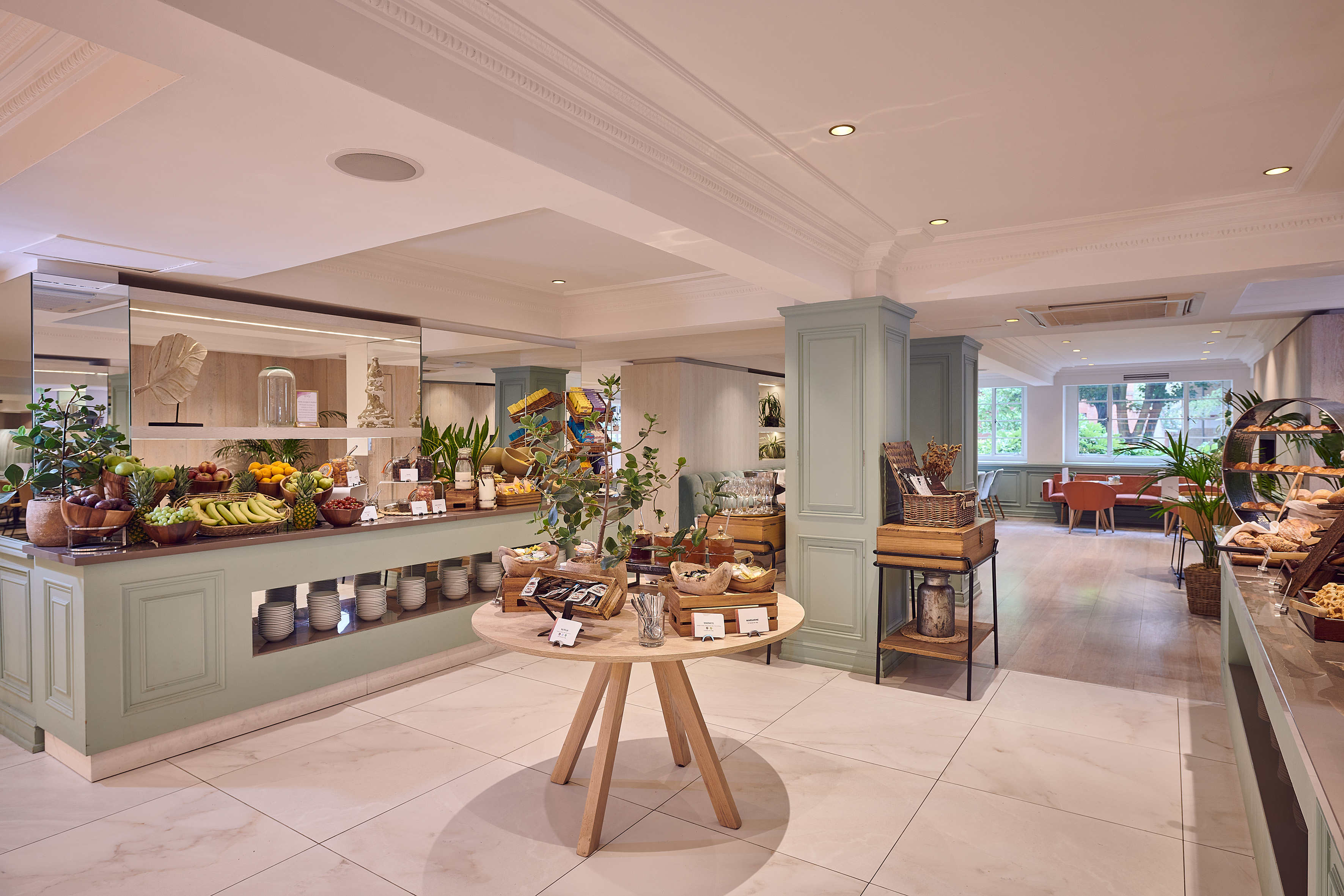 Bright hotel breakfast buffet with fresh fruit, pastries, and spacious dining area.