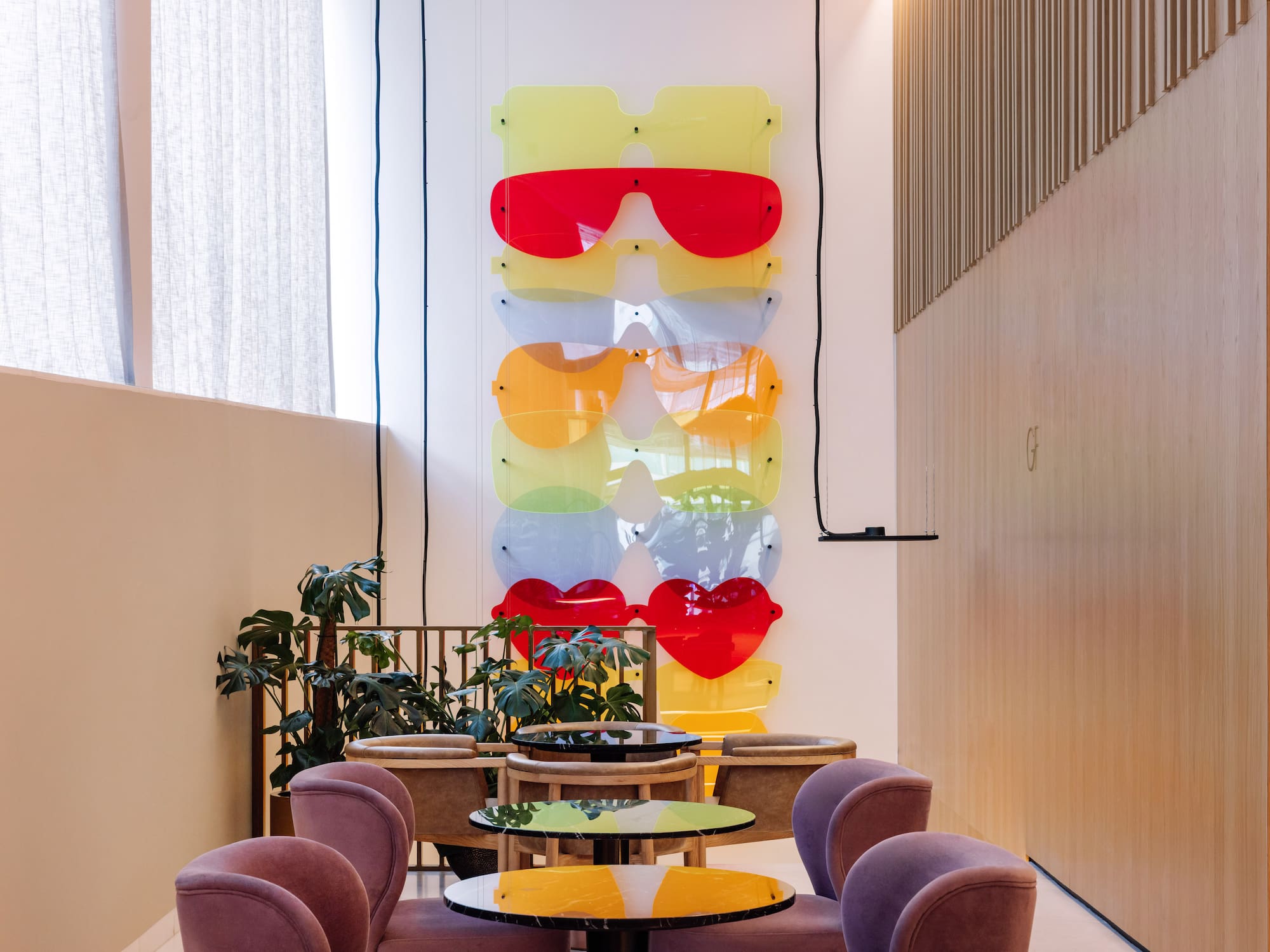Colorful oversized sunglasses wall art in a modern lounge with purple chairs.
