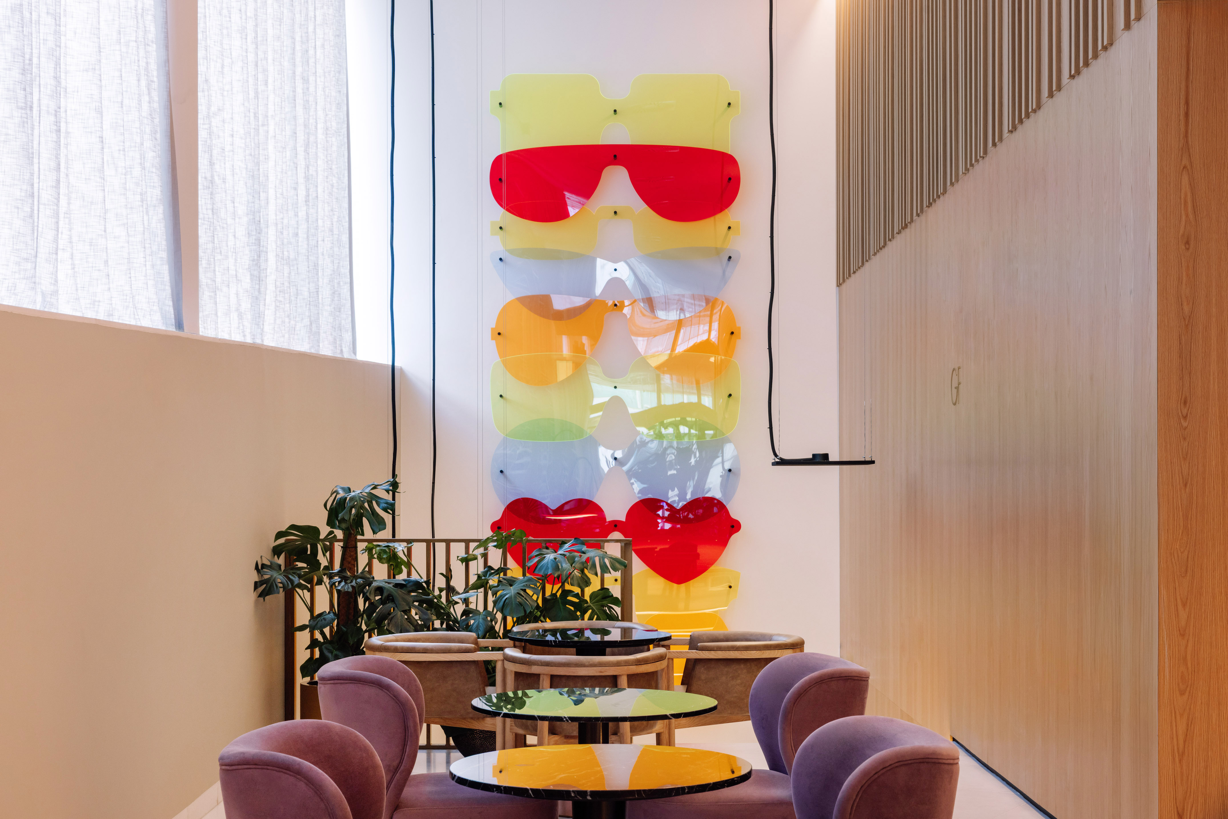 Colorful oversized sunglasses wall art in a modern lounge with purple chairs.