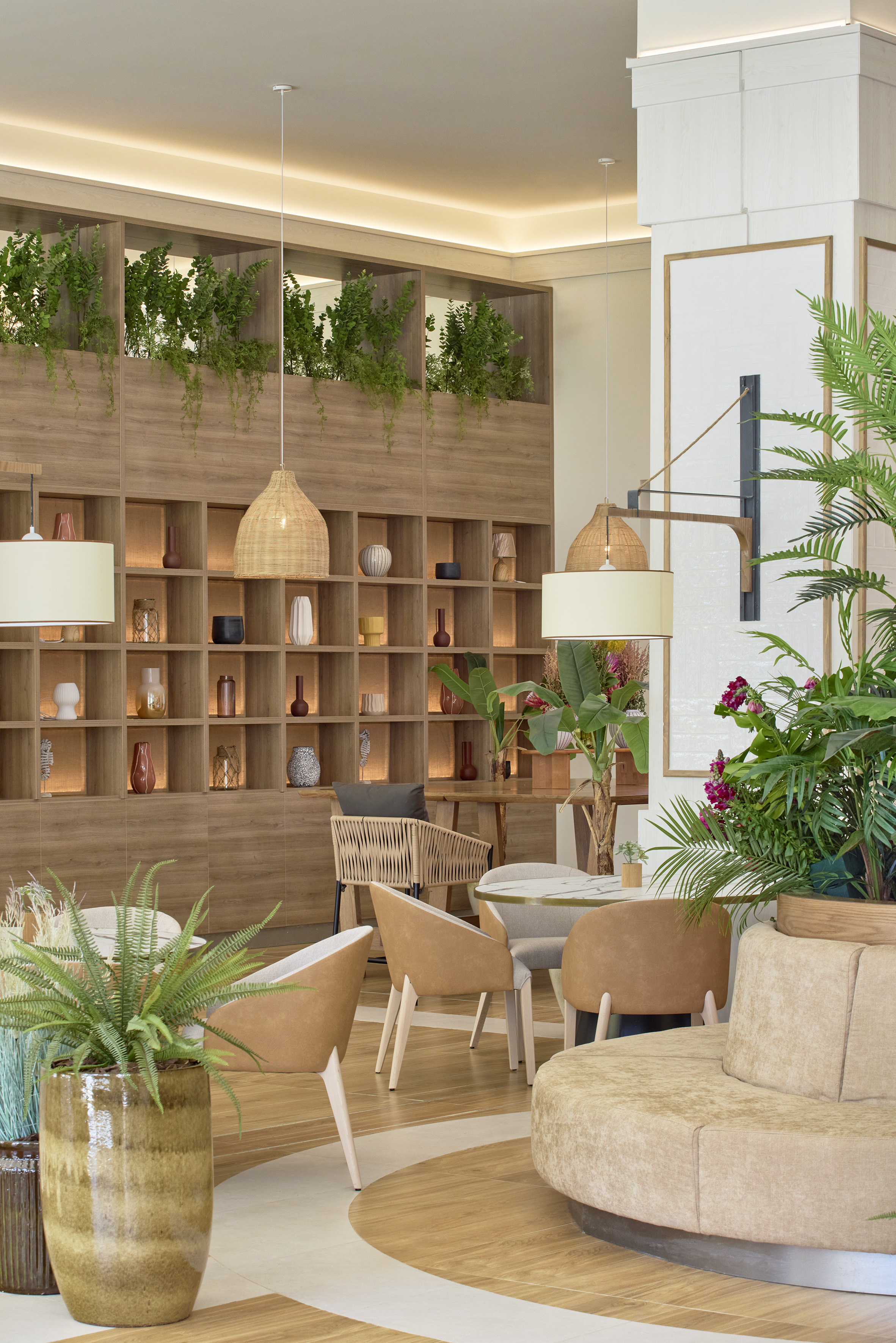 Modern cafe lounge with wooden shelves, plants, rattan lights, and cozy seating.