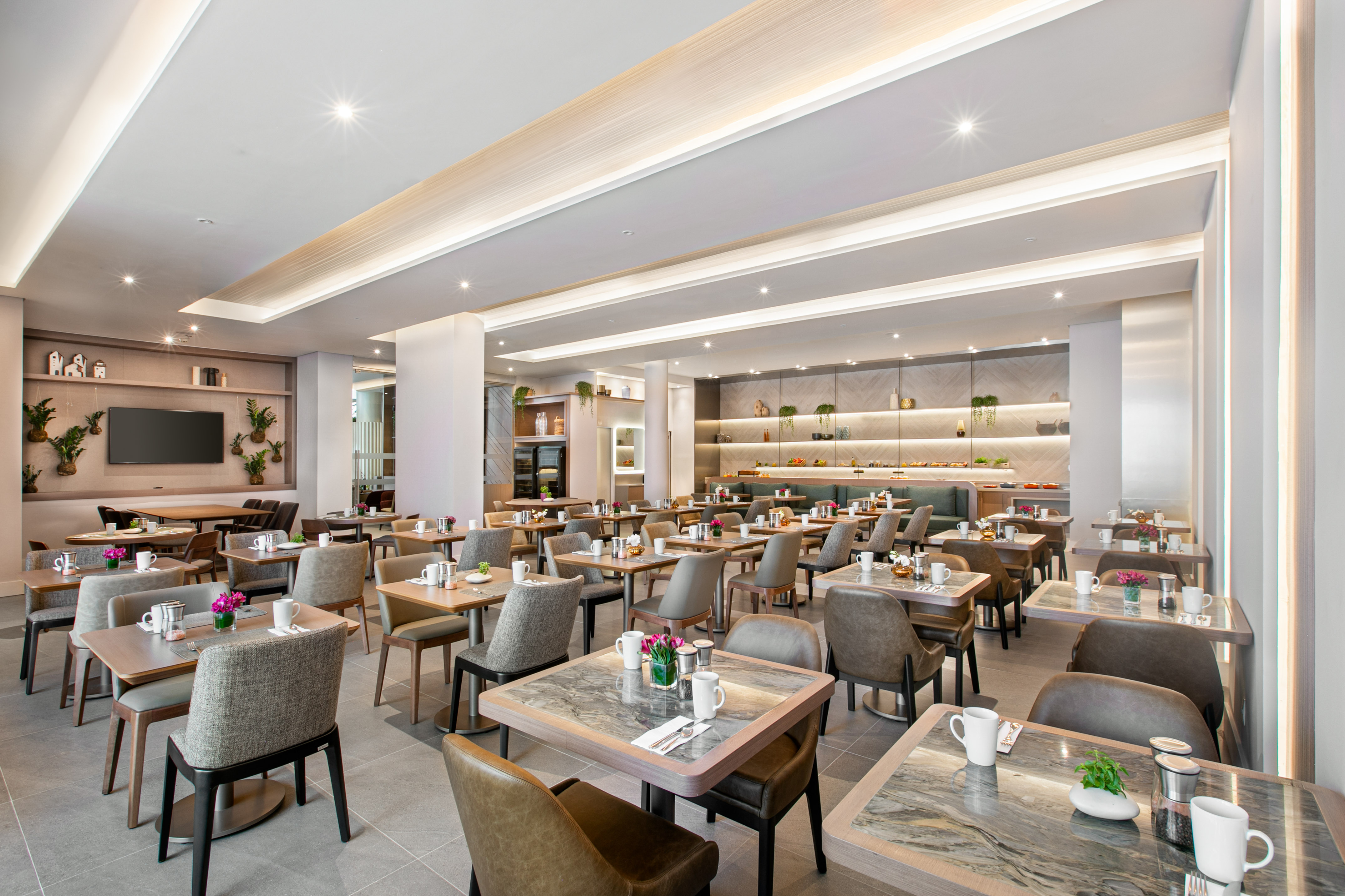 Modern hotel restaurant with buffet, dining tables, contemporary lighting.