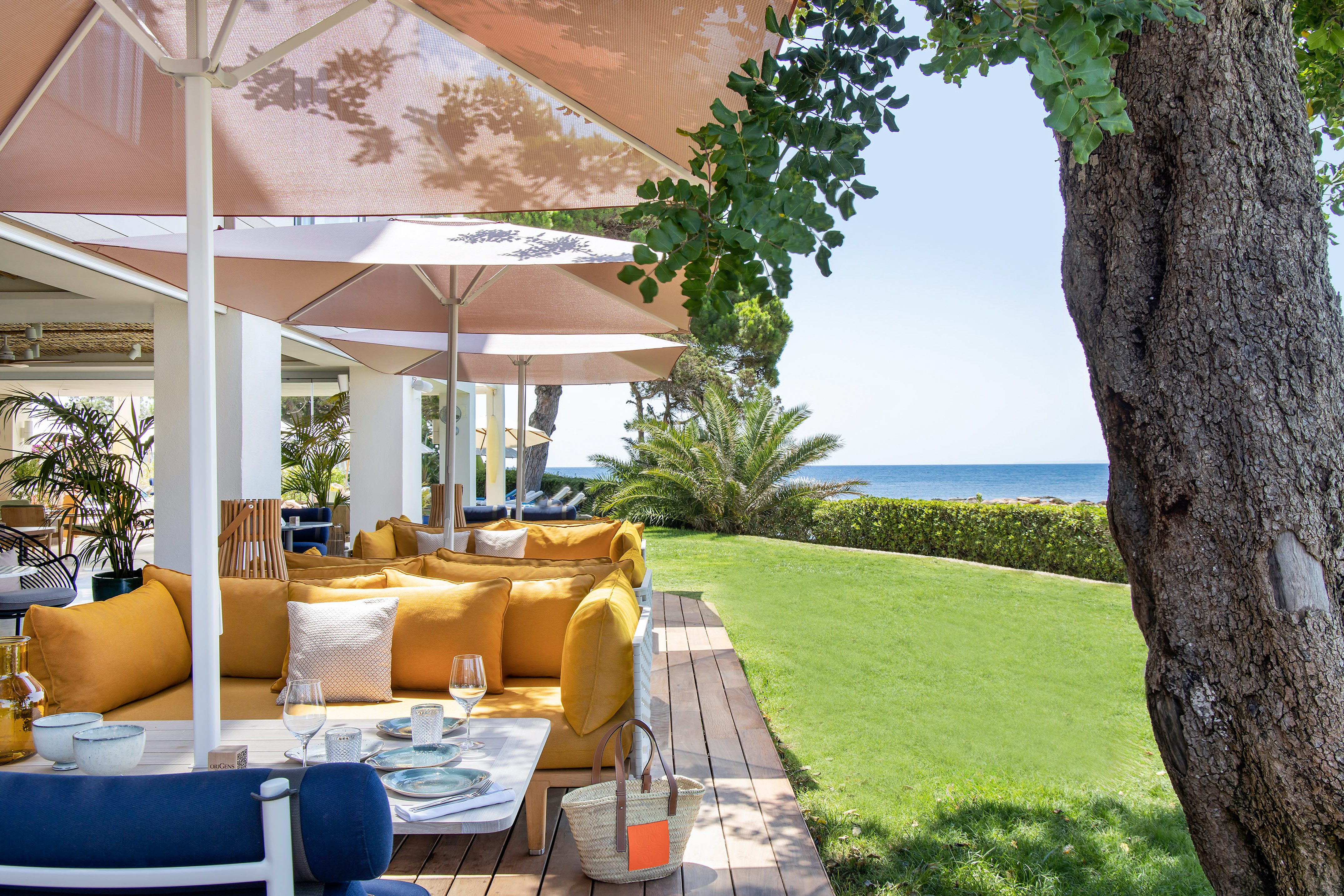 Outdoor restaurant patio with yellow seating, ocean view, and umbrellas.