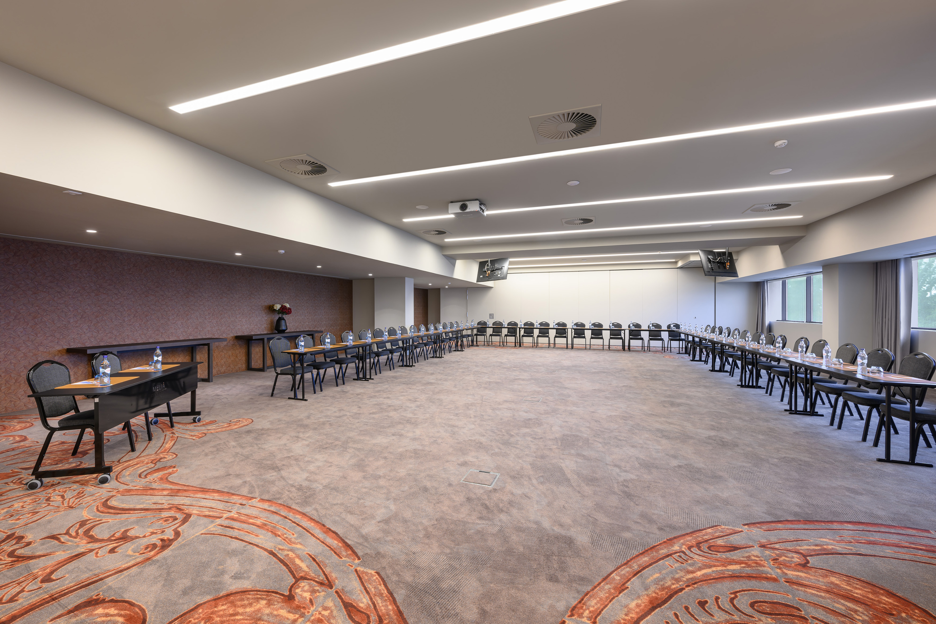 Empty hotel conference room with horseshoe table setup and modern amenities.