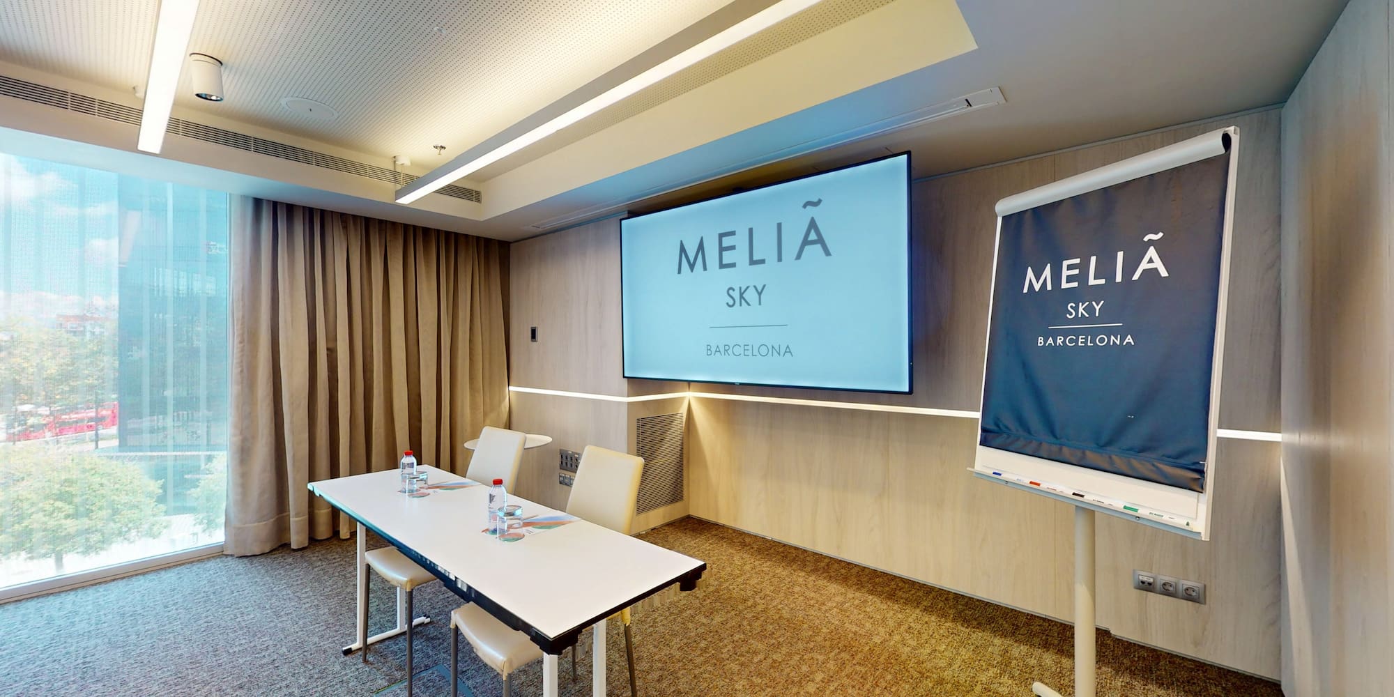 Meliã Sky Barcelona meeting room with screen, table, and flip chart.