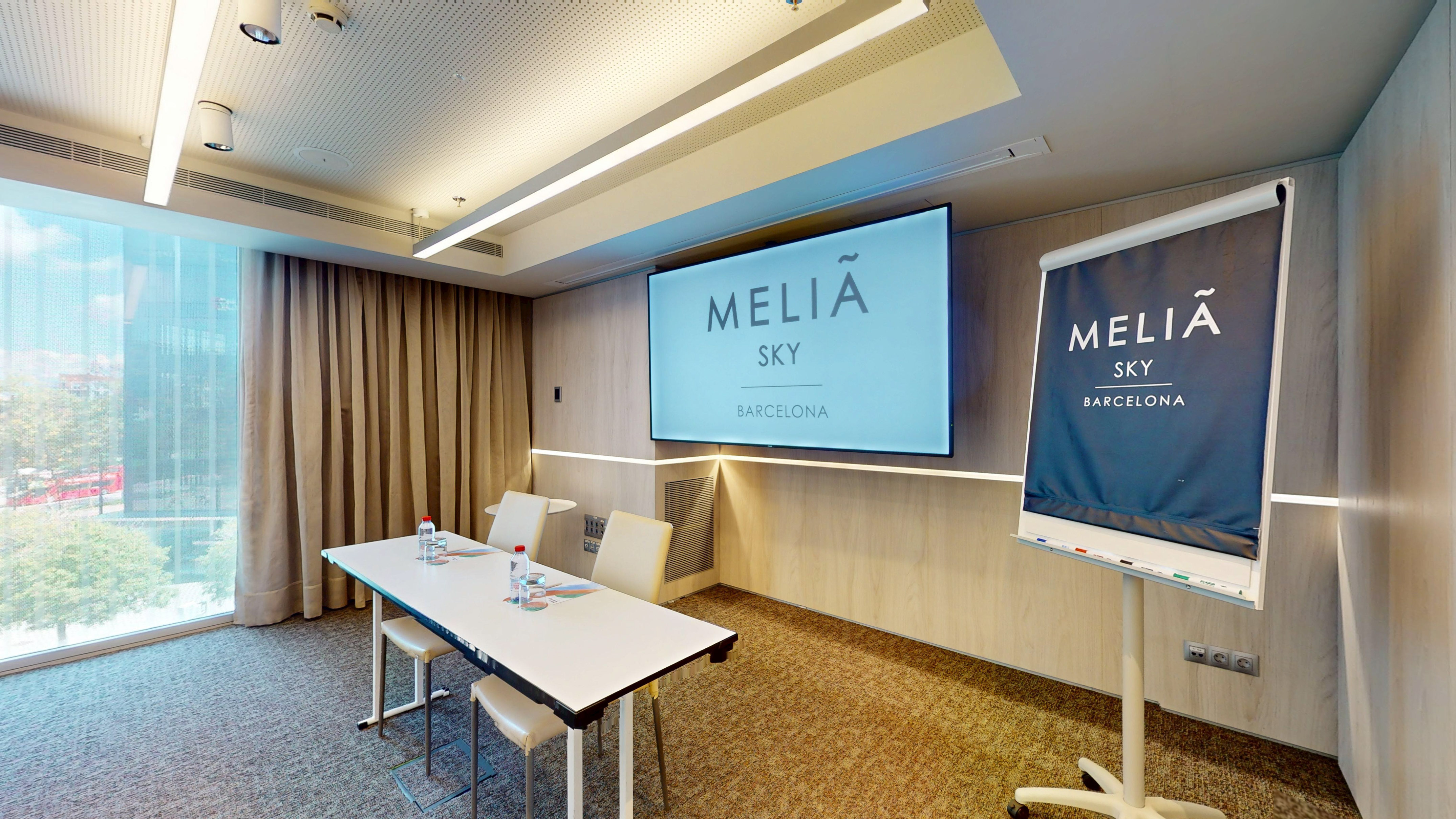 Meliã Sky Barcelona meeting room with screen, table, and flip chart.