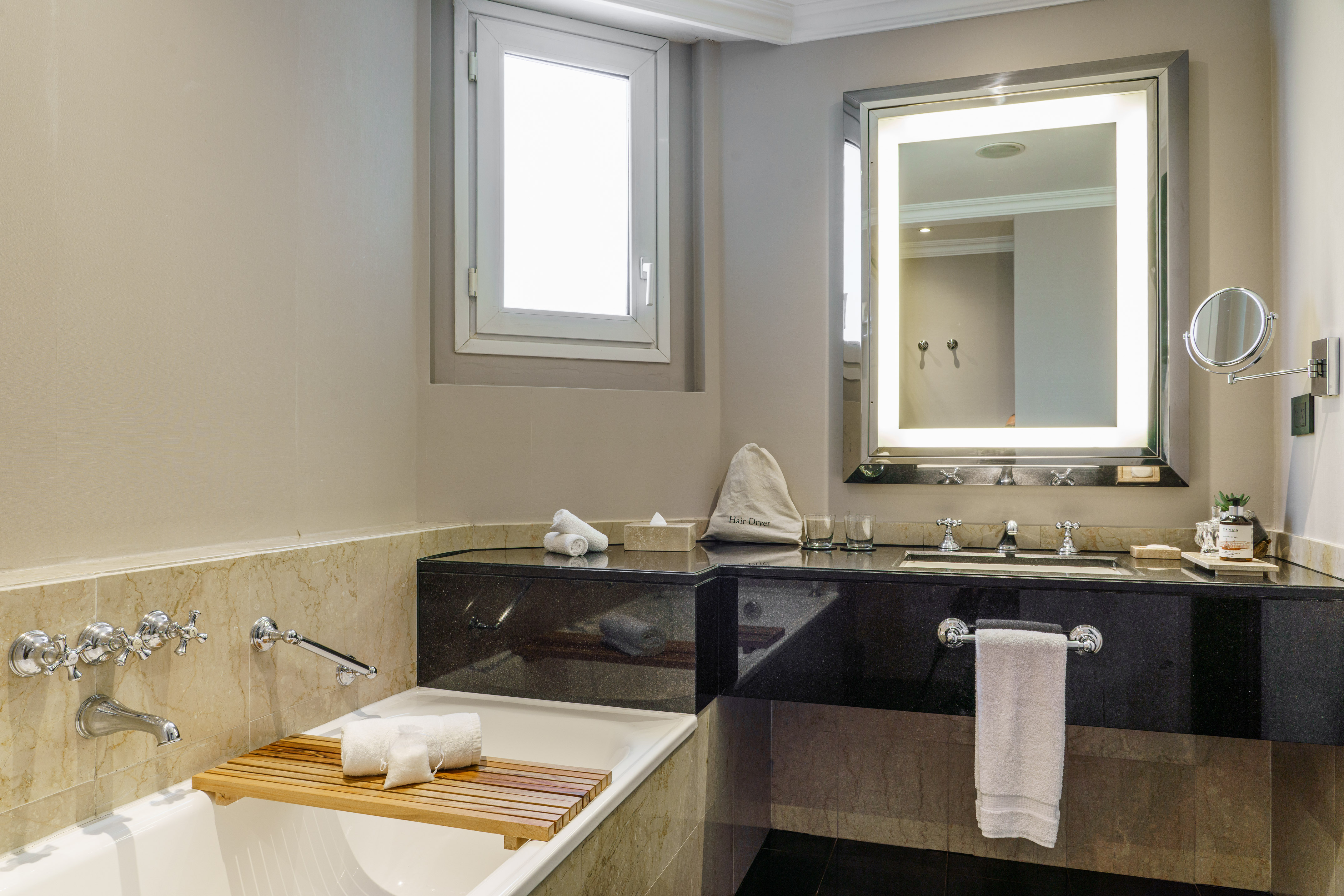 Luxury hotel bathroom with bathtub, black granite vanity, and illuminated mirror.