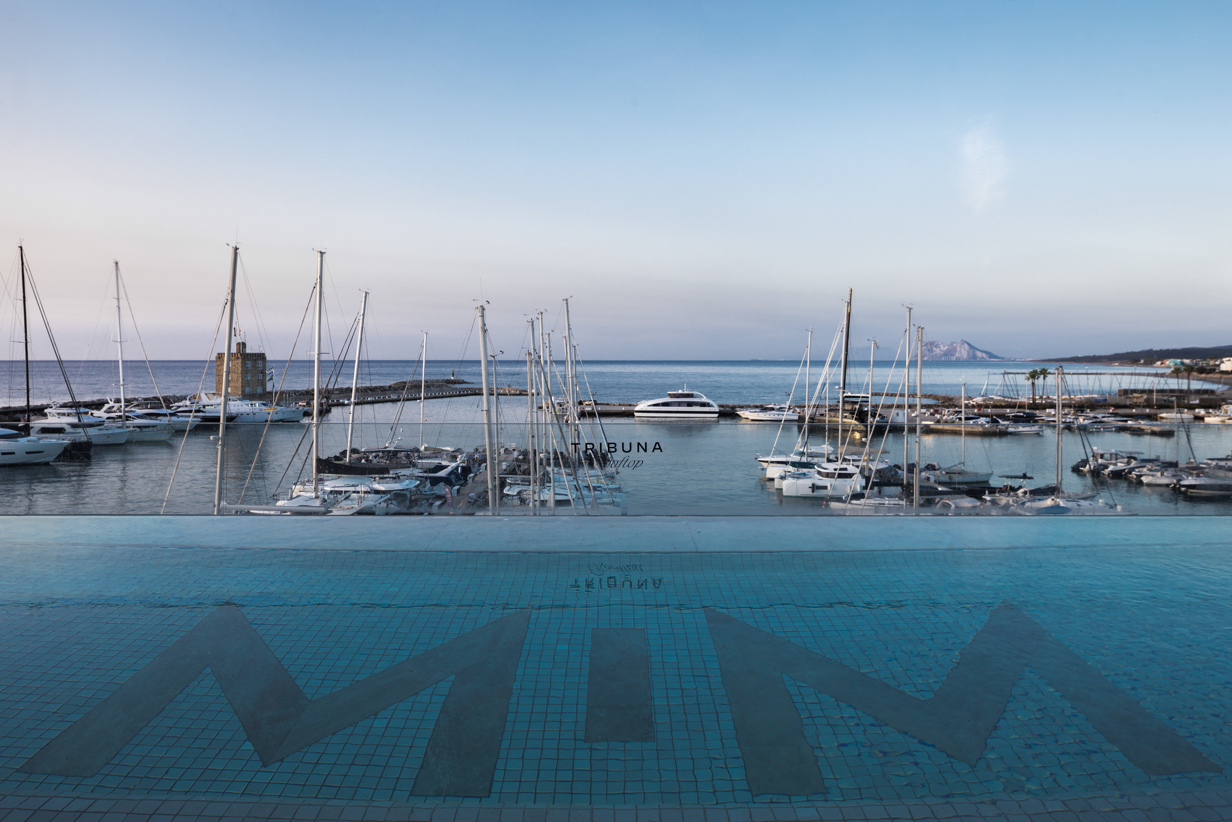 Infinity pool view of yacht marina, sailboats, and coastal fort.