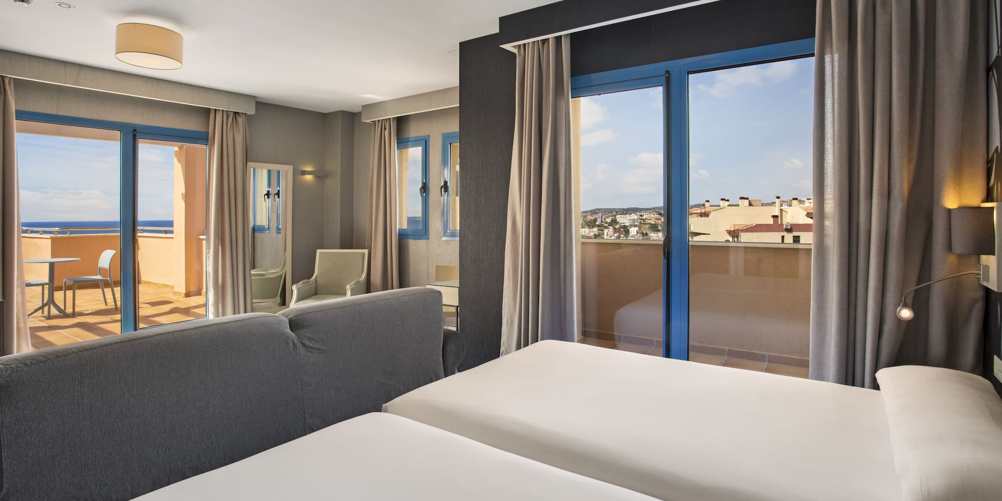 Modern hotel room with twin beds, two balconies showing ocean and city views.