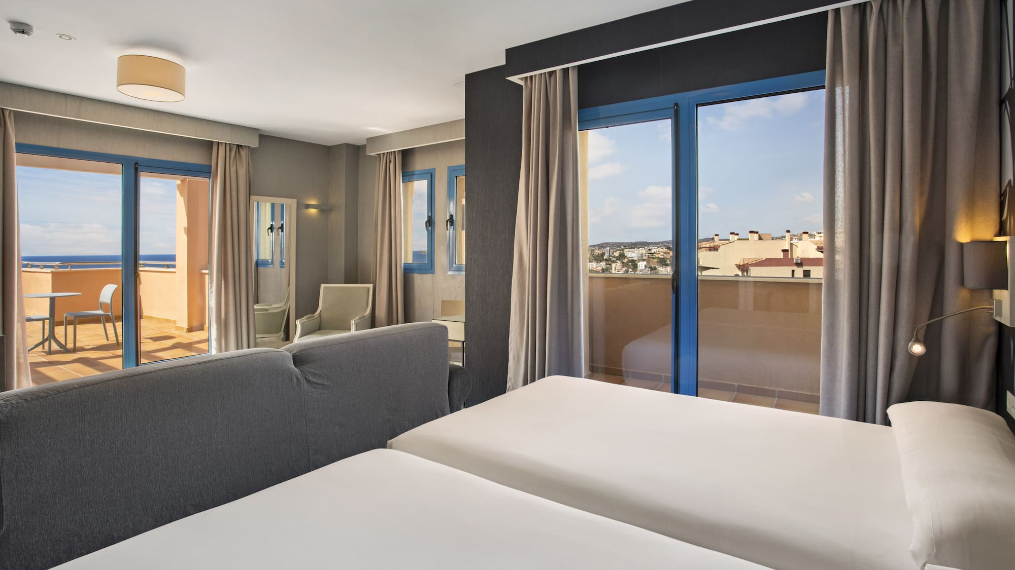 Modern hotel room with twin beds, two balconies showing ocean and city views.