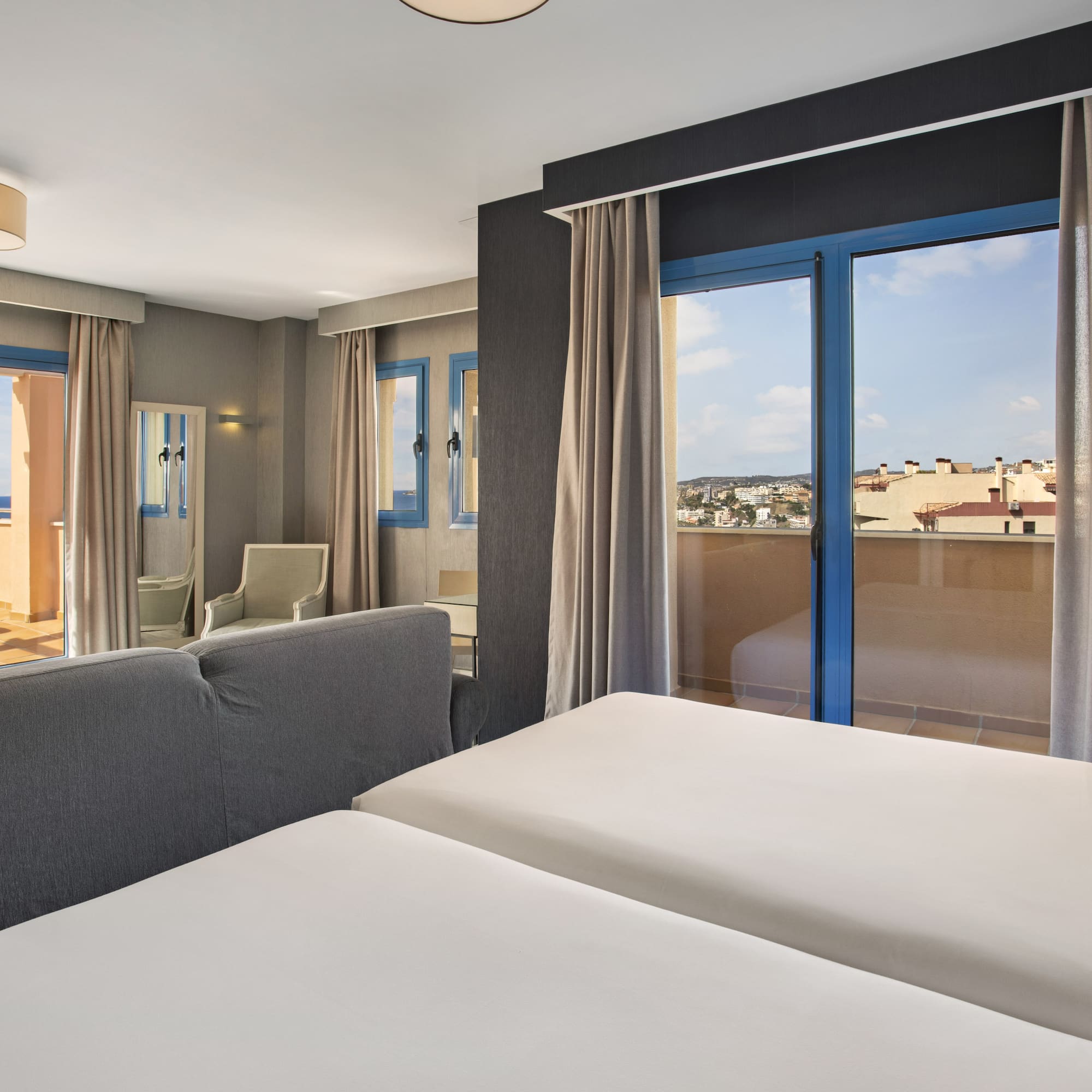 Modern hotel room with twin beds, two balconies showing ocean and city views.